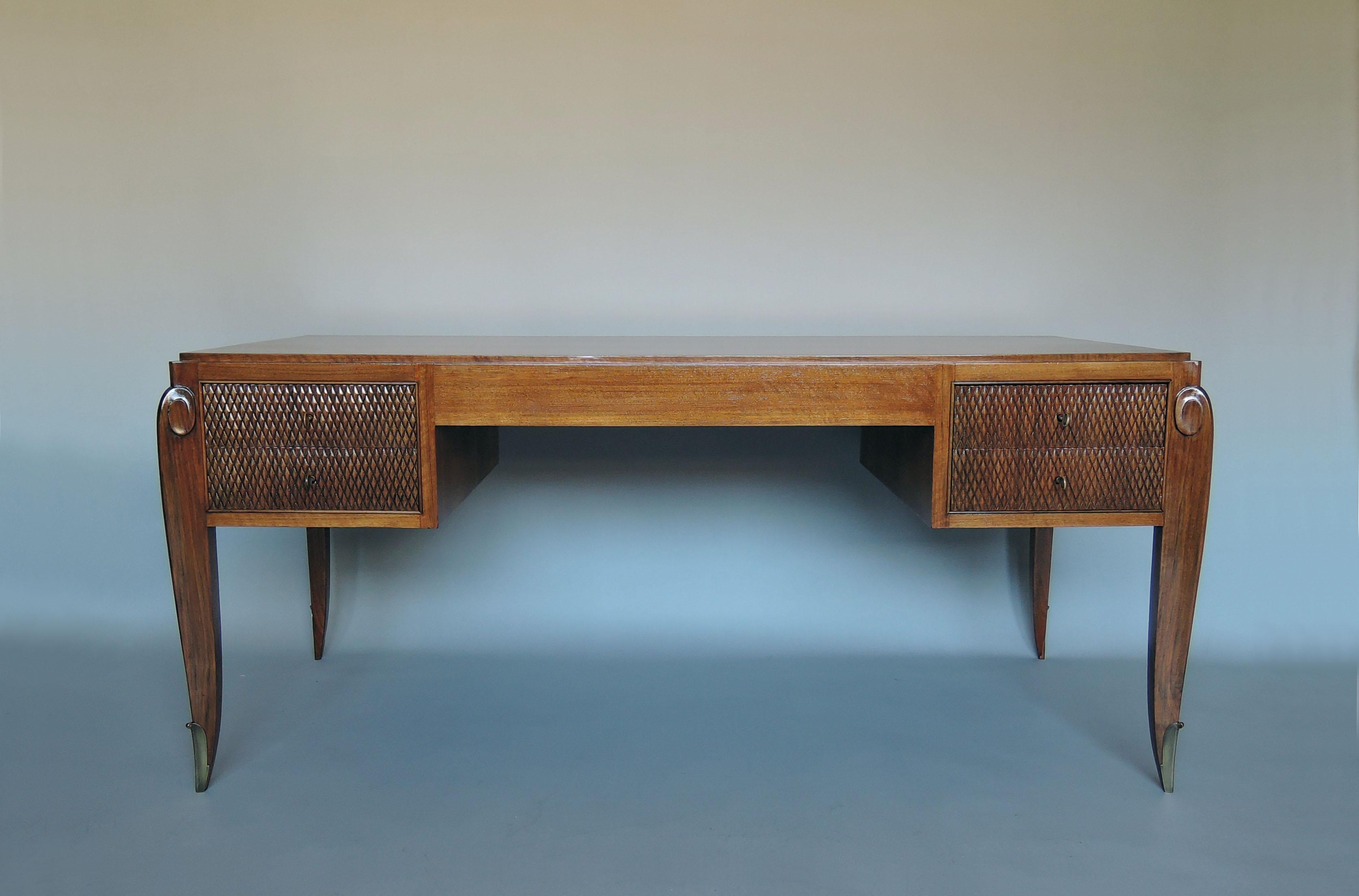 Jean Pascaud (1903-1996) - Feiner französischer Art Déco-Schreibtisch mit vier Schubladen aus Nussbaumholz, geschnitztem Rautenmuster und vier Rollenbeinen mit Bronzesockeln.

Der passende 3-türige Schrank mit einer raffinierten Messingintarsie von