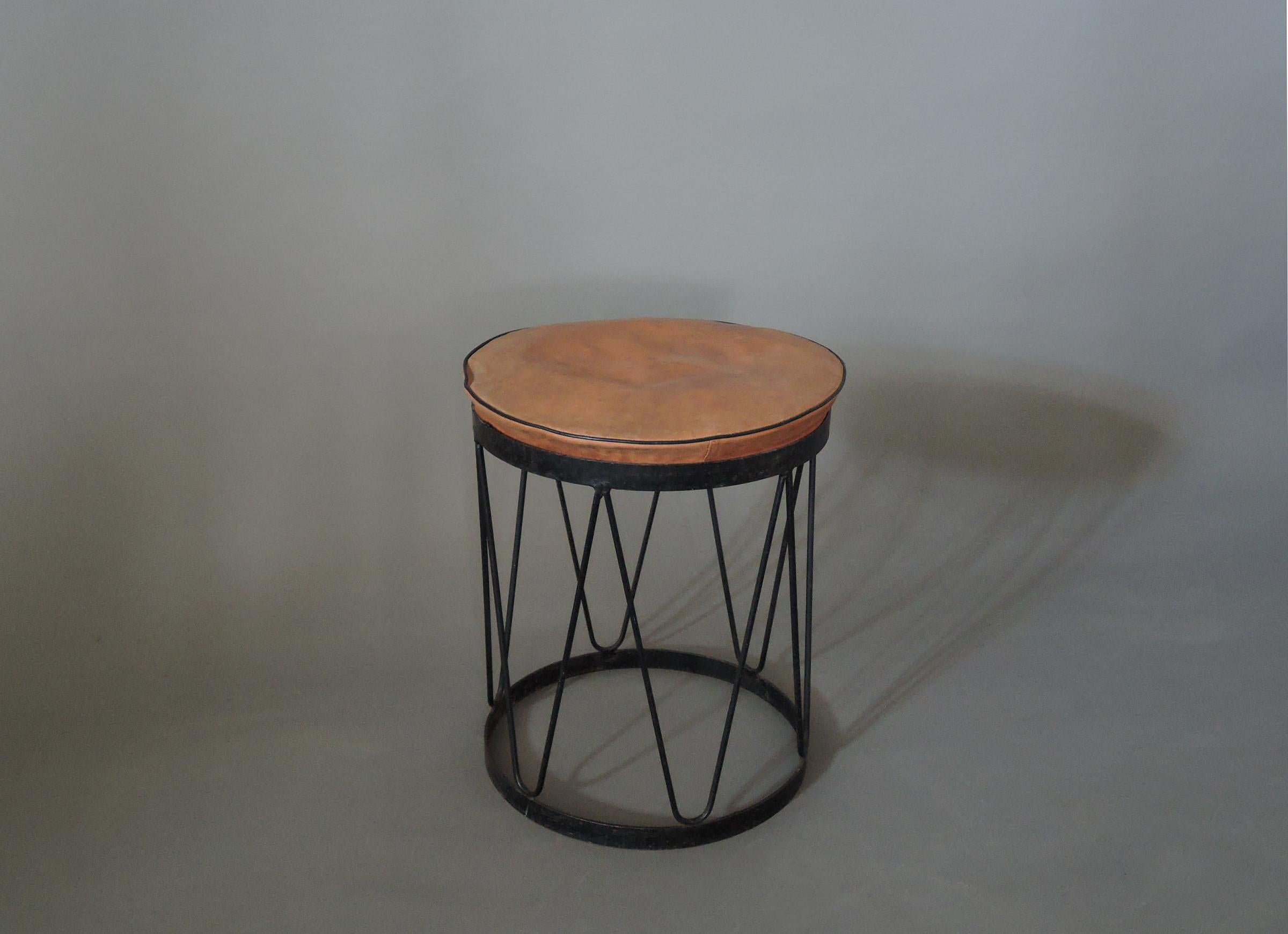 A fine French mid-century round stool with a black lacquered metal base and a leather cushion.