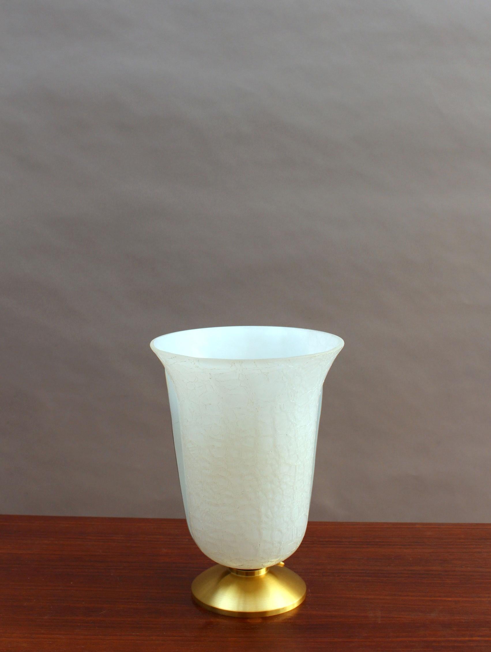 With a round brass base that supports a white crazed glass and brass tulip-shaped shade.
Signed.