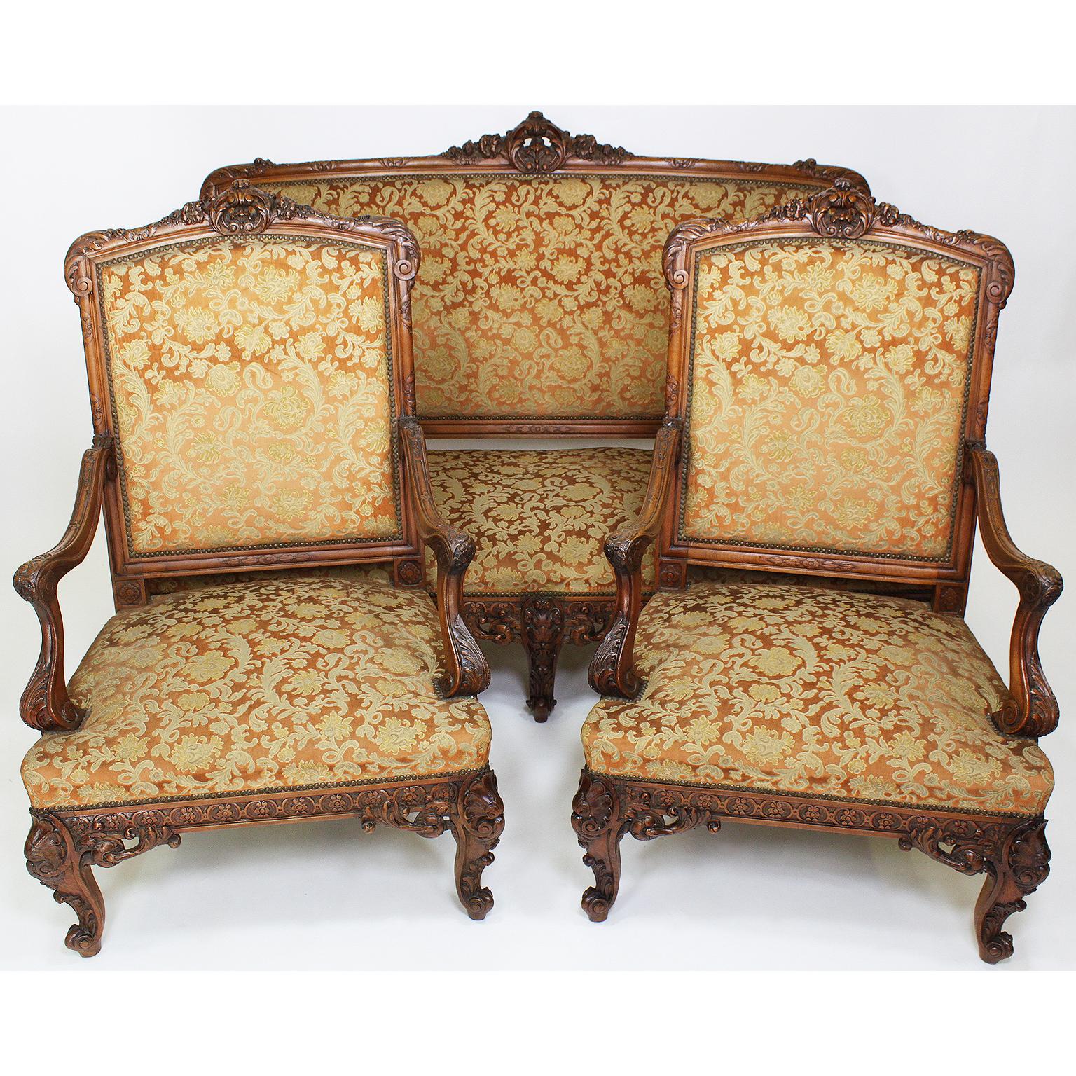 A fine and large French 19th century Louis XV style carved walnut three-piece salon suite. The high back intricately carved frames with floral and wreath design, comprising of a three-corps settee and two armchairs, all with open and padded armrests