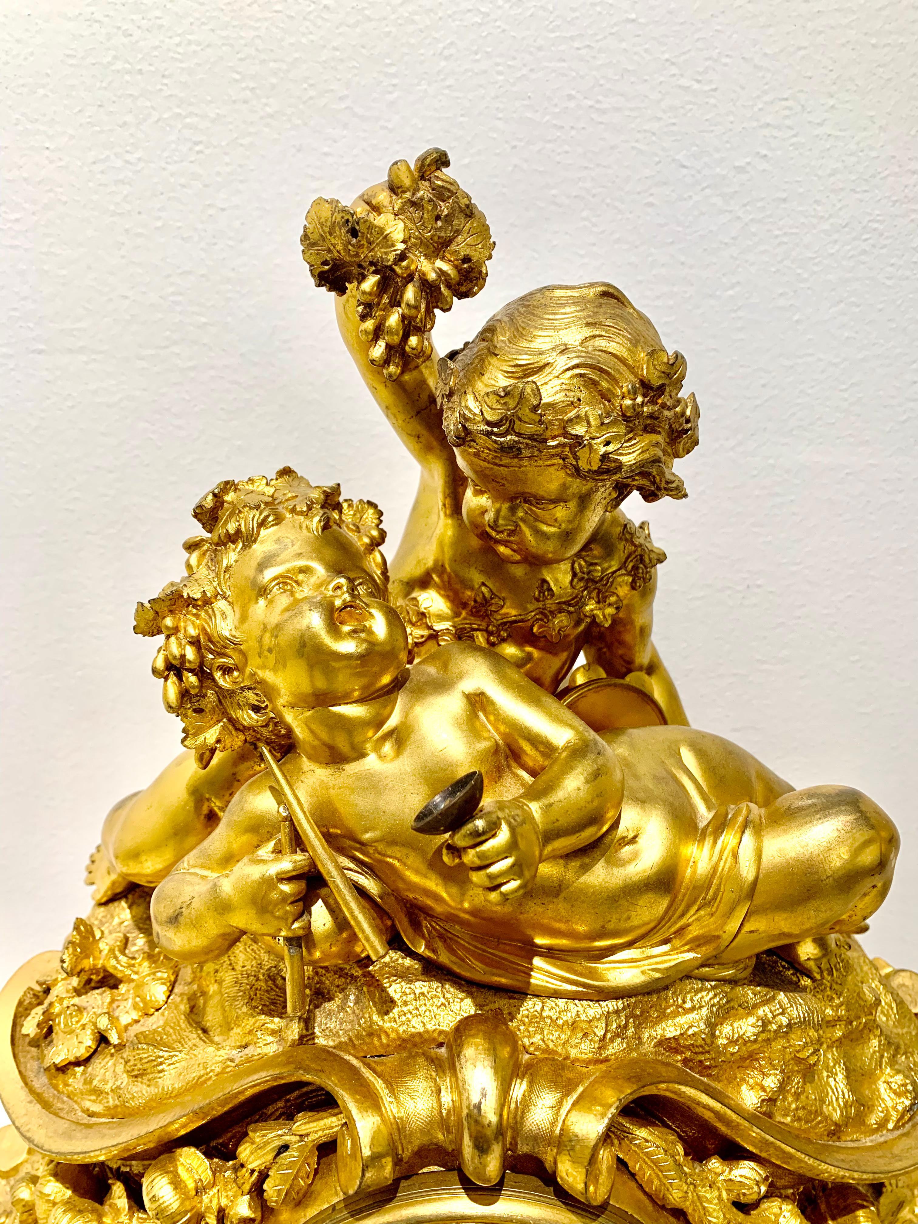 Fine French 19th century gilt bronze figural Louis XV style clock. The crest showing a pair of Bacchanale subject putti, one reclining on a naturalistic rocky outcropping with a chalice in one hand and a pair of batons in the other, while the second