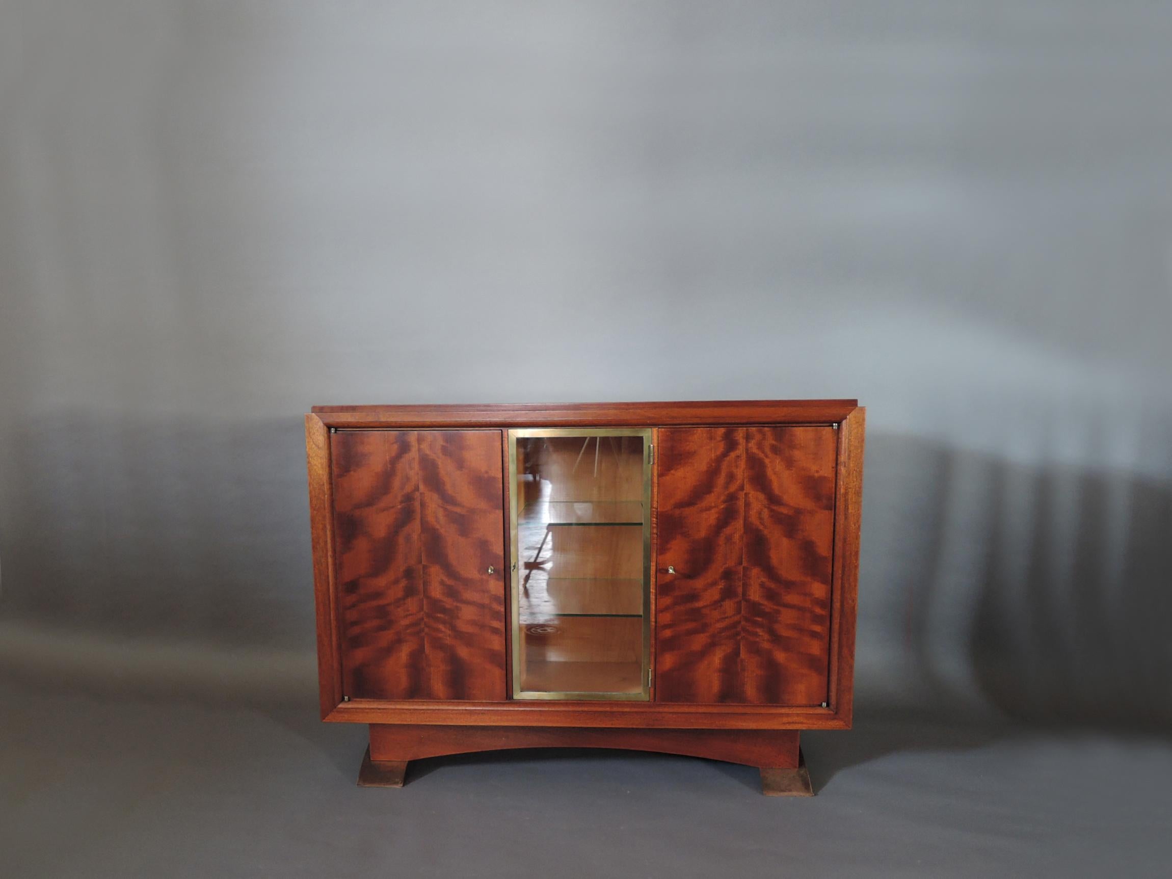 Albert-Lucien Guenot (1894-1993): A fine French Art Deco mottled mahogany cabinet with 1 central glass door in a bronze frame flanked by two wood doors; with bronze feet.
Edited by Pomone.
    