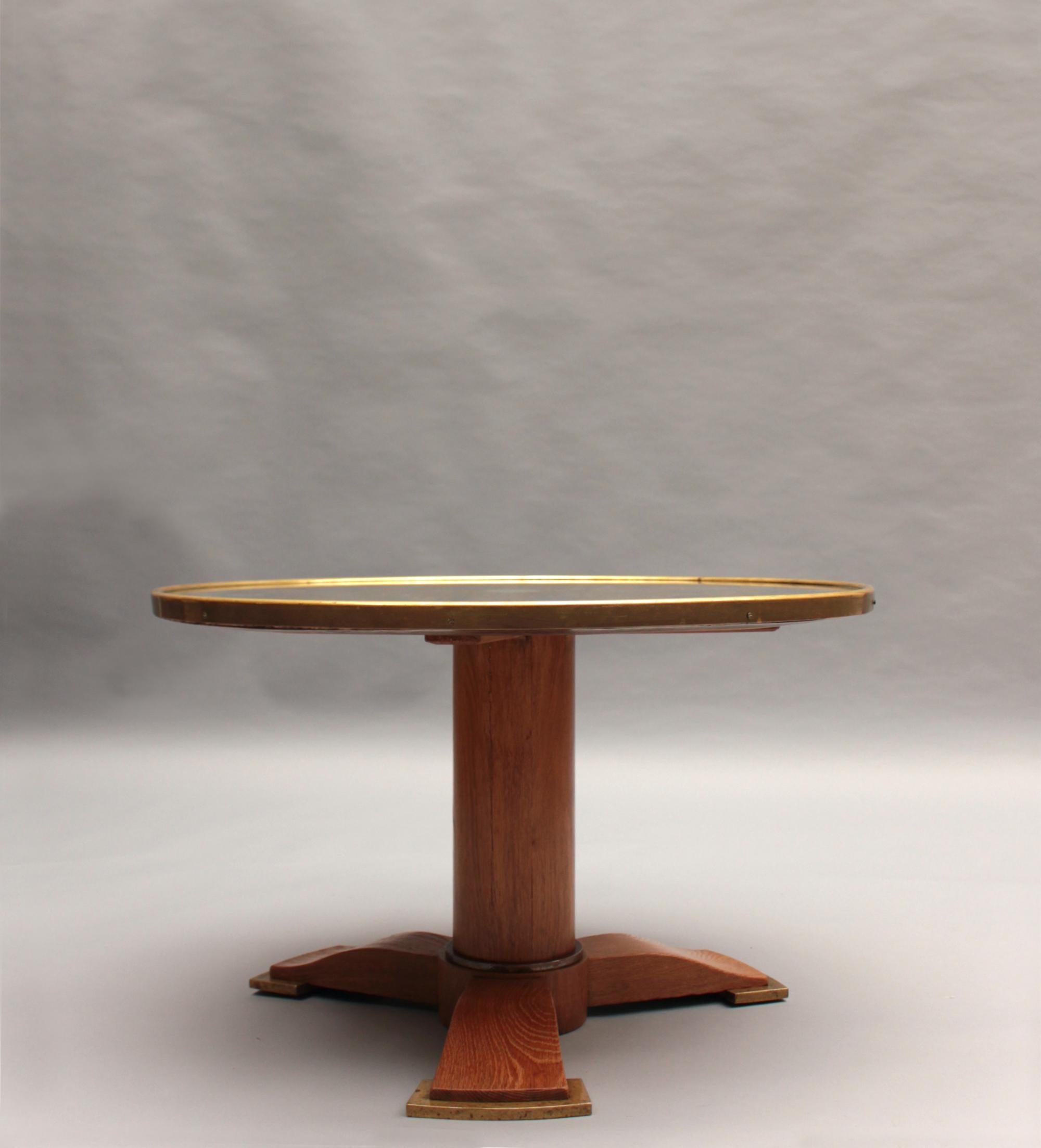 Jules Leleu (1883-1961) - Fine table basse française Art déco à plateau miroir en églomisé rond encadré d'un anneau de bronze, sur un piédestal tripode cylindrique en chêne à trois pieds légèrement galbés reposant sur des pieds en bronze.  
 