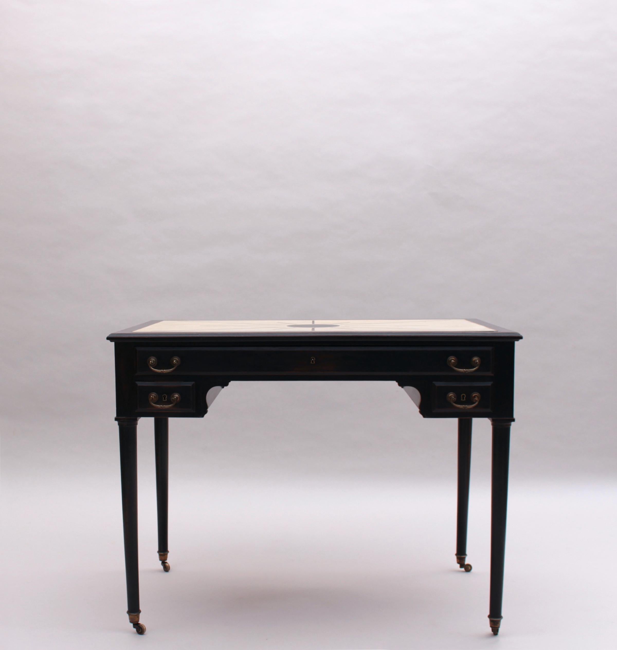 A fine French blackened wood desk with 3 drawers, an off white & black lacquered top with metal Inlays, and bronze handles and wheels.