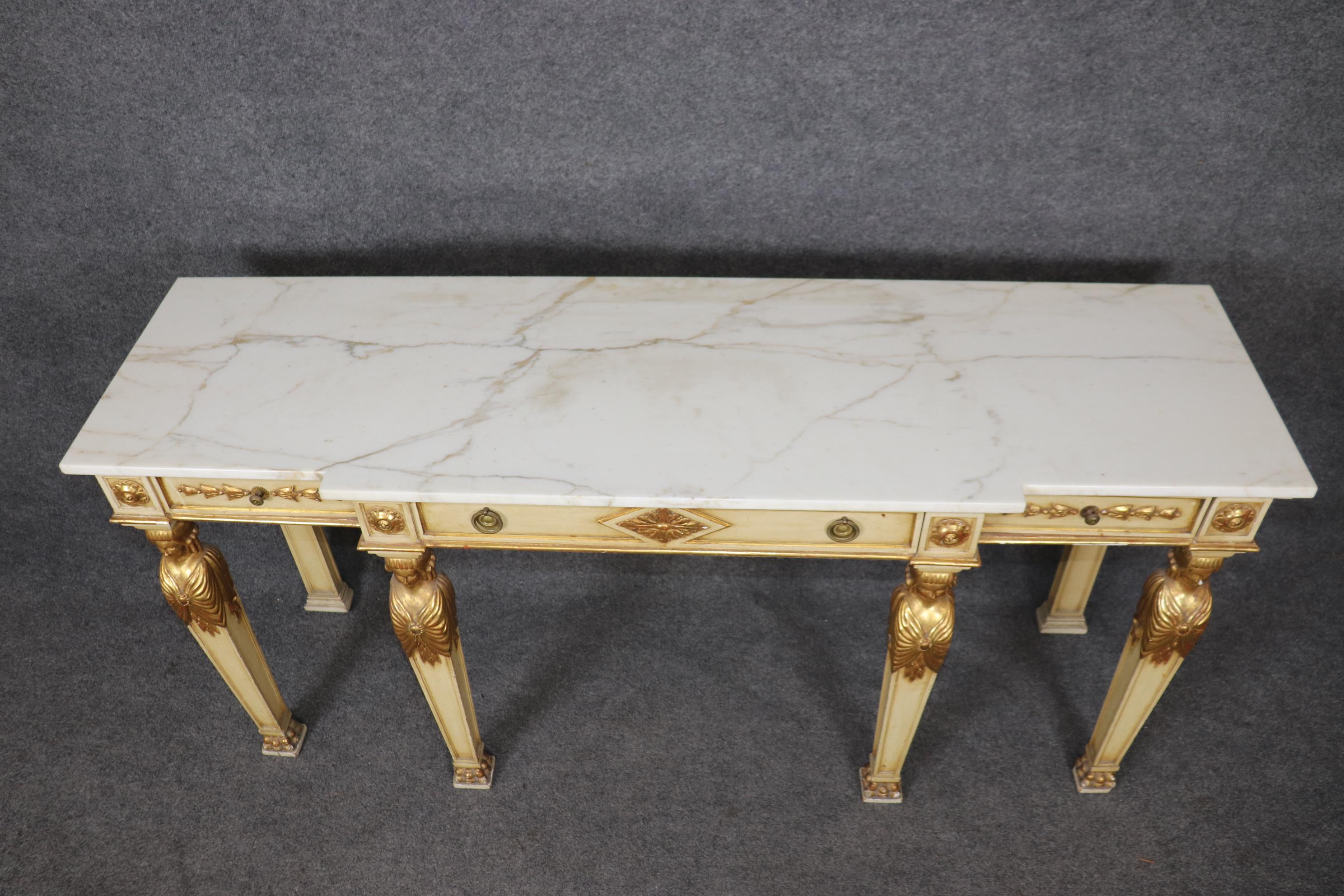 This is a beautifully carved and decorated gilt and creme painted French Empire style console or sofa table. The table features beautifully carved figures in gold leaf and a beautiful slab of marble on top. The table does show minor signs of age and