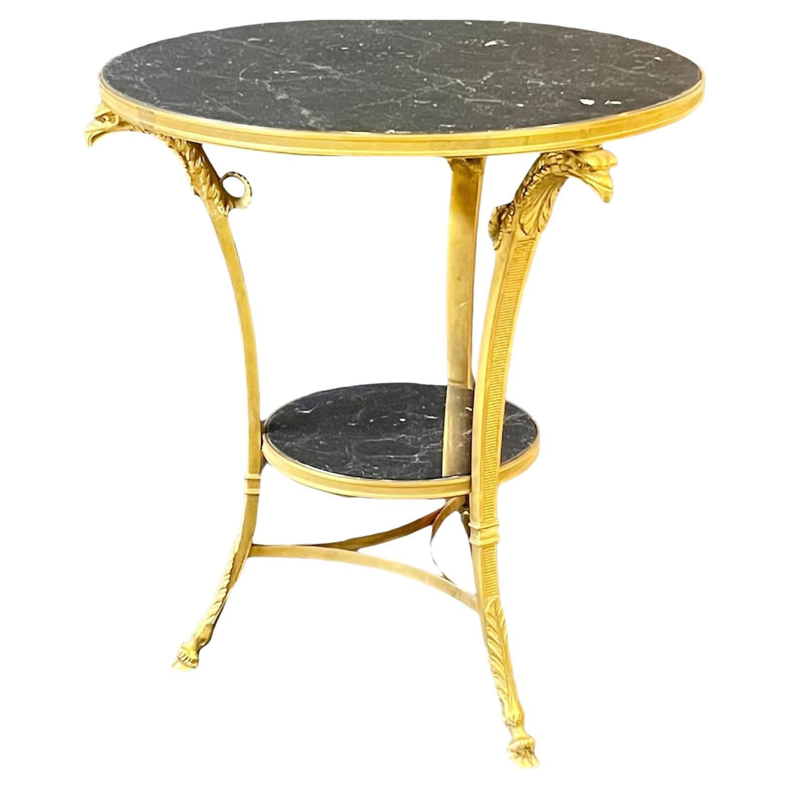 Très belle table guéridon de style Empire français du début du XXe siècle en bronze doré et marbre. Un plateau circulaire en marbre noir veiné de blanc est maintenu par un bandeau décoratif nervuré. Le cadre en bronze doré est composé de trois pieds