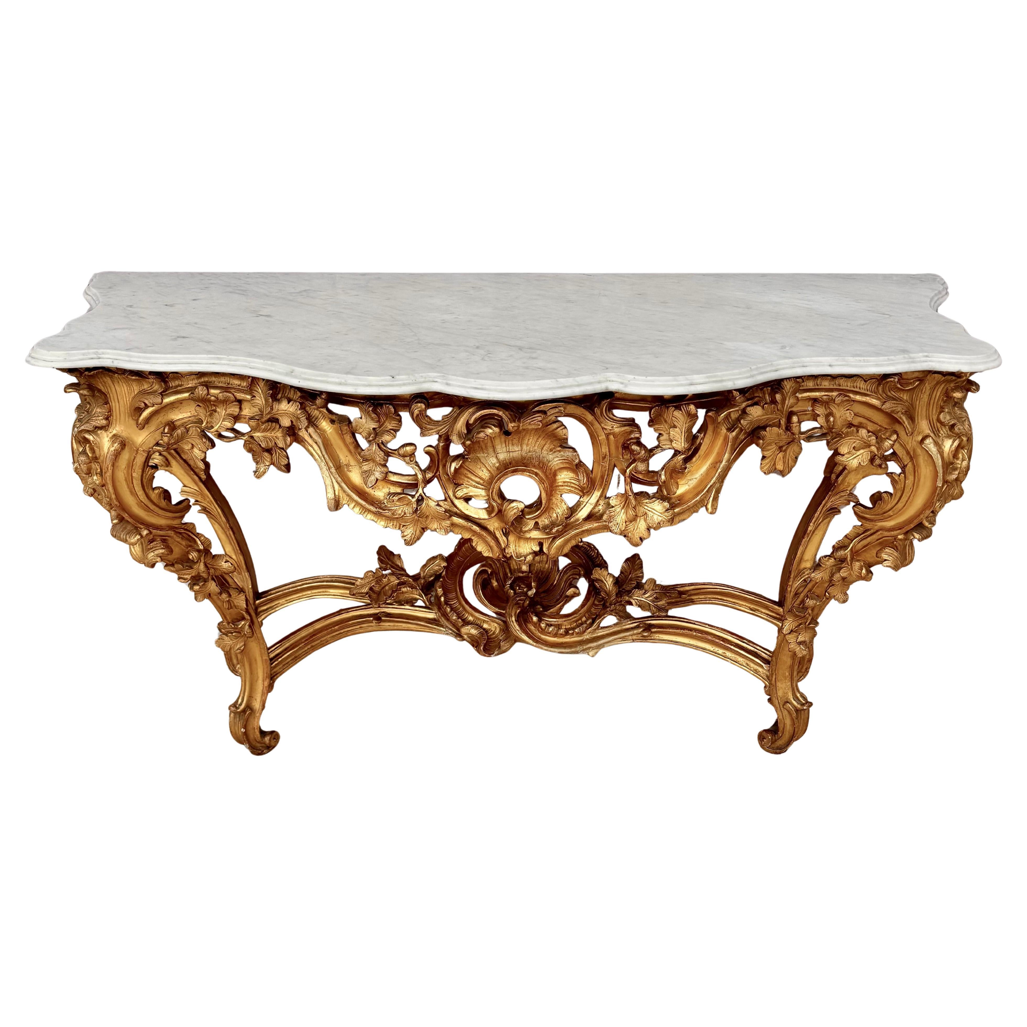 Un raffinato tavolo da console in legno dorato in stile Rococo Luigi XV con il piano originale in marmo di Cararra sopra una cornice in legno dorato con angoli arrotondati che presenta un fregio intricato intagliato con una conchiglia centrale e