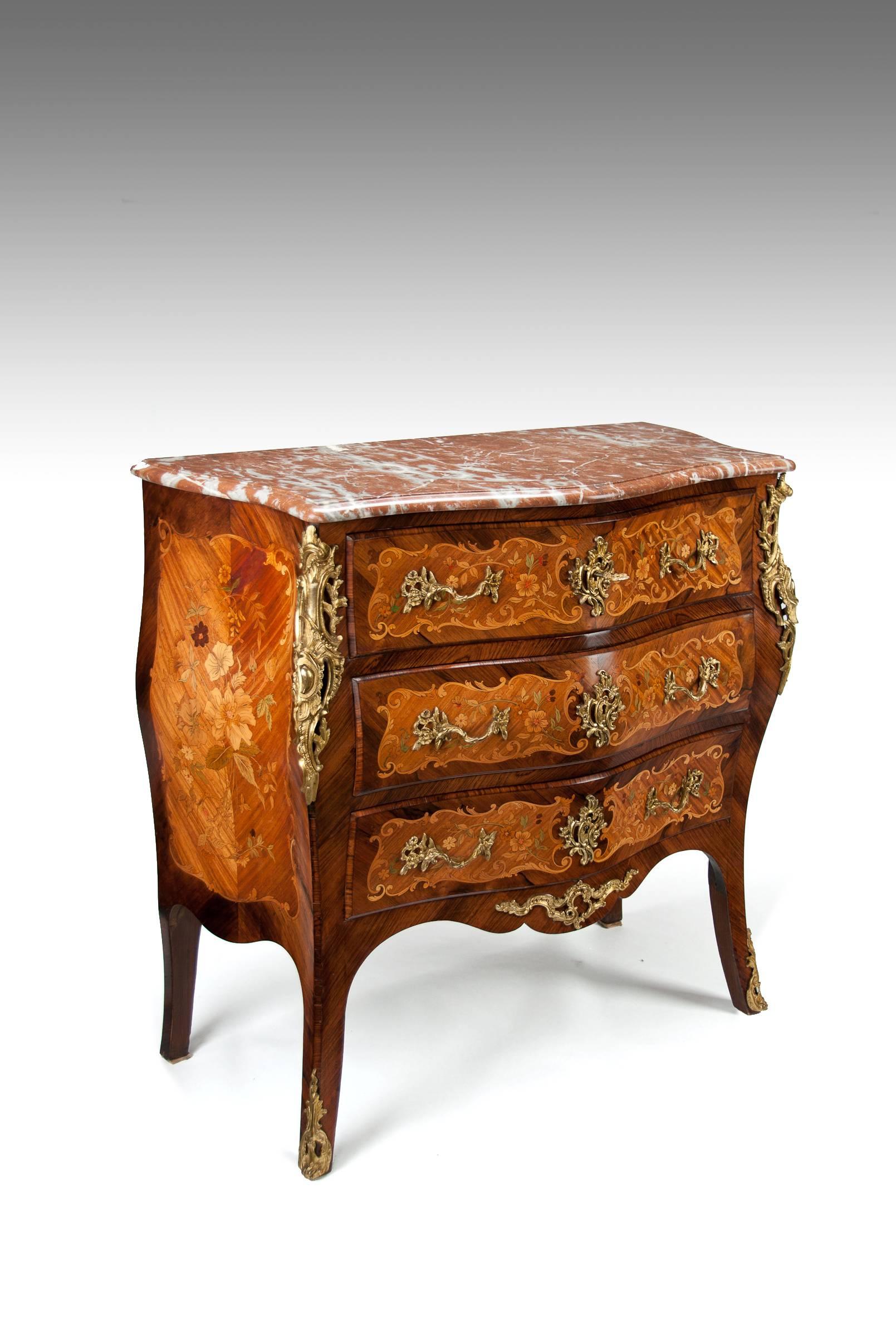 A fine quality antique French rosewood and kingwood floral marquetry inlaid pink marble topped bombe commode in the Louis XV Manner dating to circa 1910-1920.
This very well executed commode with finely inlaid marquetry panels has a serpentine