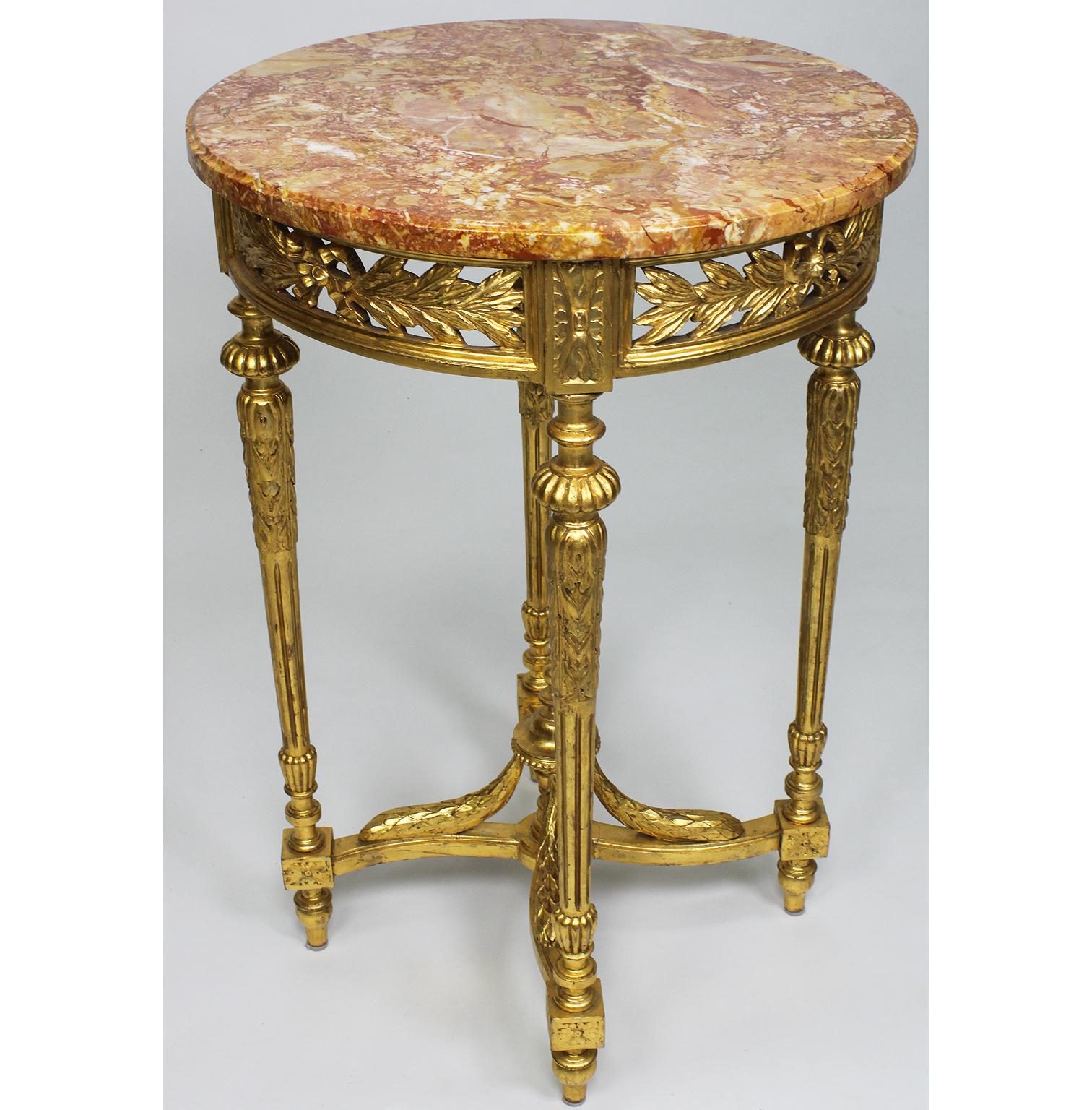 A French Louis XVI Style Gilt Wood Carved Guéridon Side Table with Marble Top. The circular gilt wood carved apron with an acanthus tied leaf wreath, raised on four fluted carved legs conjoined with a stretcher centered with an urn finial surmounted