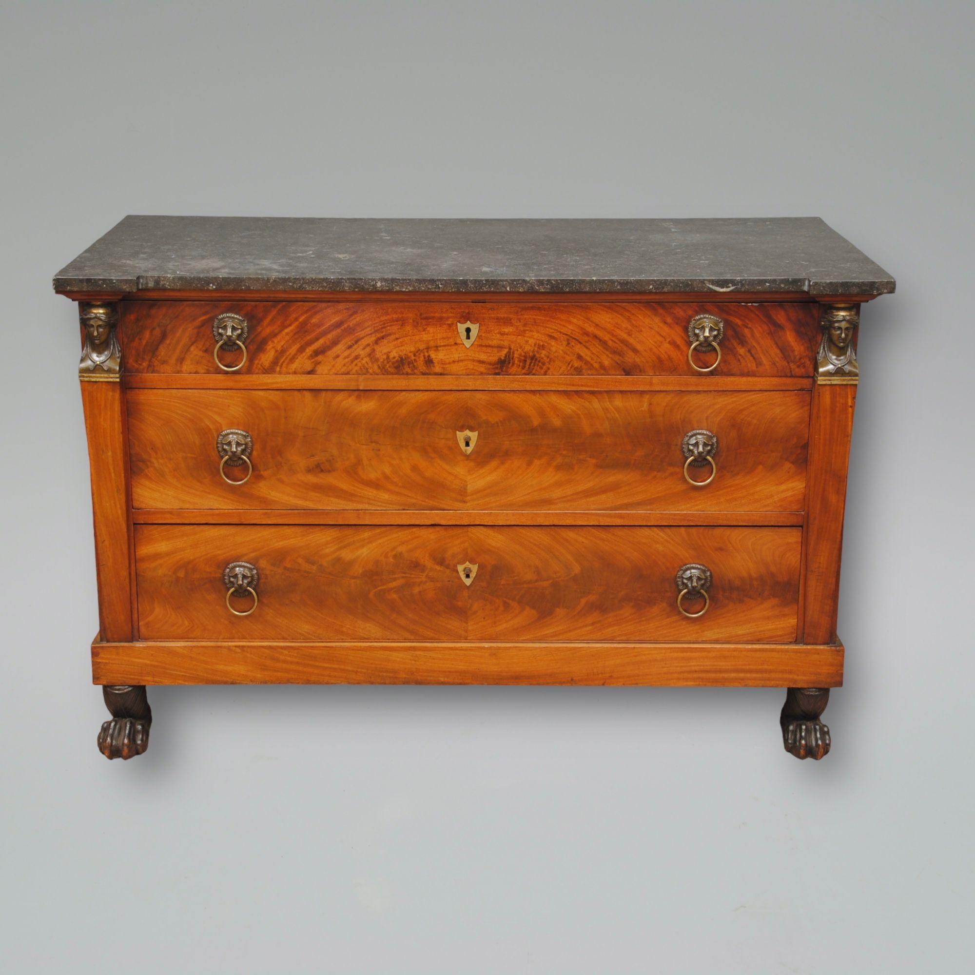 A french marbled top and bronze mounted mahogany commode. The original grey marble top over the three drawers with flame veneers and lion mask handles. The pillars either side are topped with classical heads and it stands on paw feet. Good colour