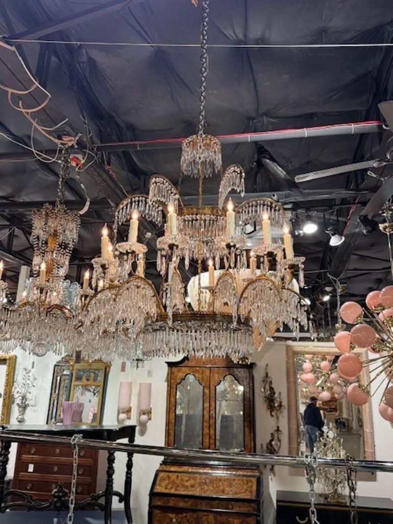 Il s'agit d'un lustre de la Maison Maison Jansen en bronze doré et cristal, datant du milieu du 20e siècle. Il présente un design luxueux typique de la Maison/One, connue pour ses pièces élégantes et de grande qualité. Le lustre est orné et