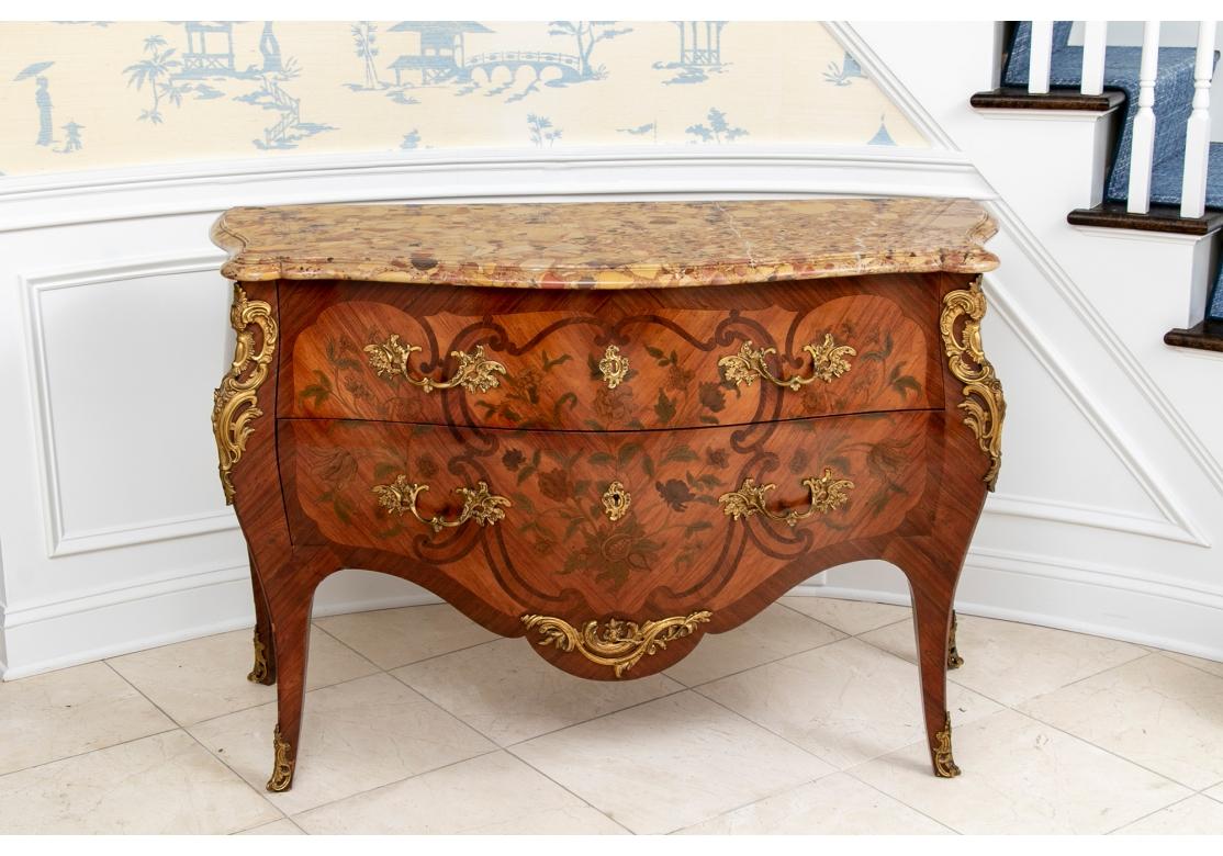 A fine and striking bombe commode with parquetry case and colored floral marquetry on the two drawers and sides. Elaborate brass baroque style leafy mounts with one working escutcheon (lacking a key) and sabots. With a fine conforming marble top