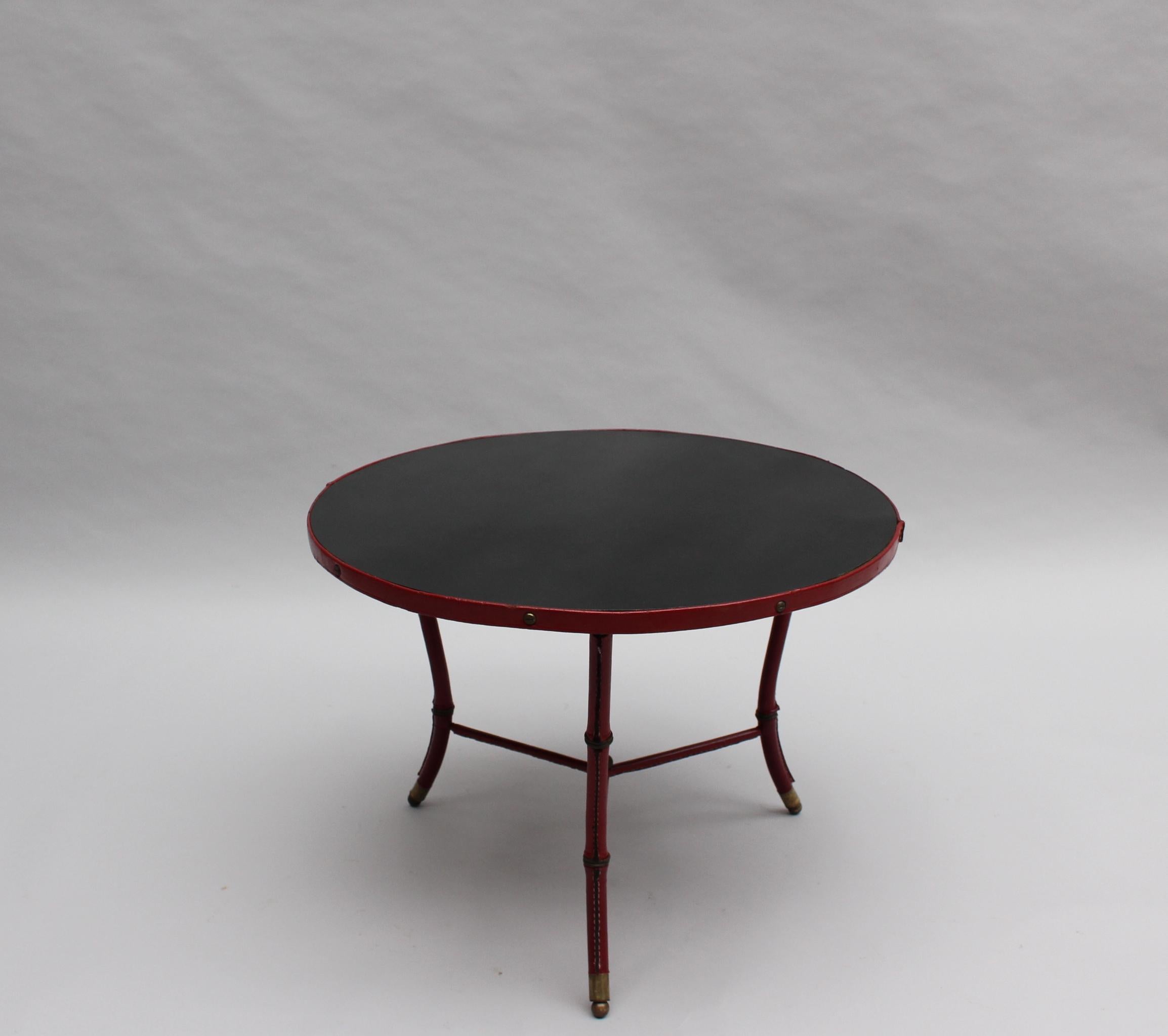 With a red leather covered three legs base, a black laminated round top and bronze details.
