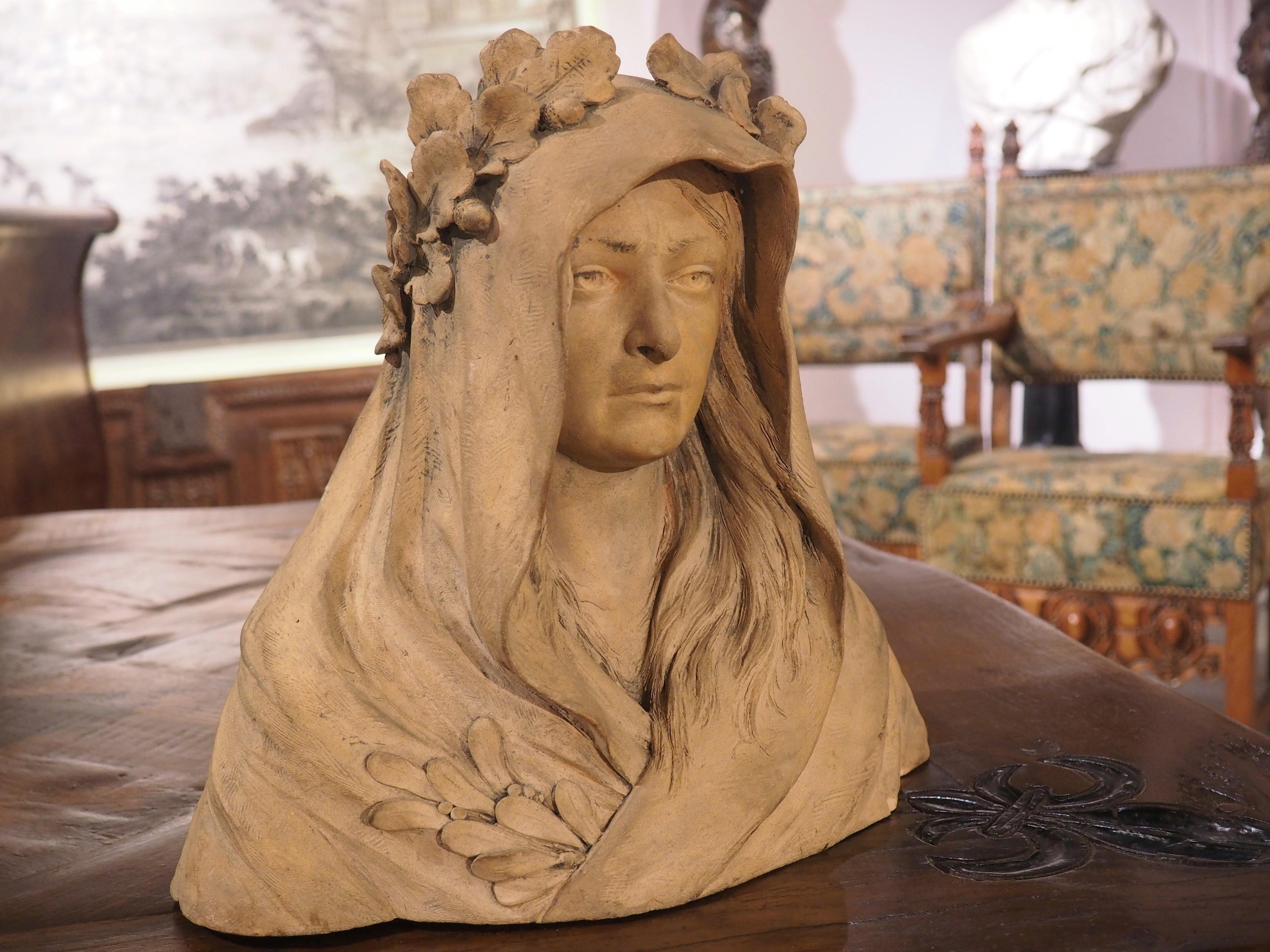 Diese Terrakotta-Büste einer Frau weist einige exquisite Details auf. Die Figur wurde Ende des 19. bis Anfang des 20. Jahrhunderts in Frankreich geschaffen und trägt langes, glattes Haar, das unter einer Kapuze hervorlugt, möglicherweise einem