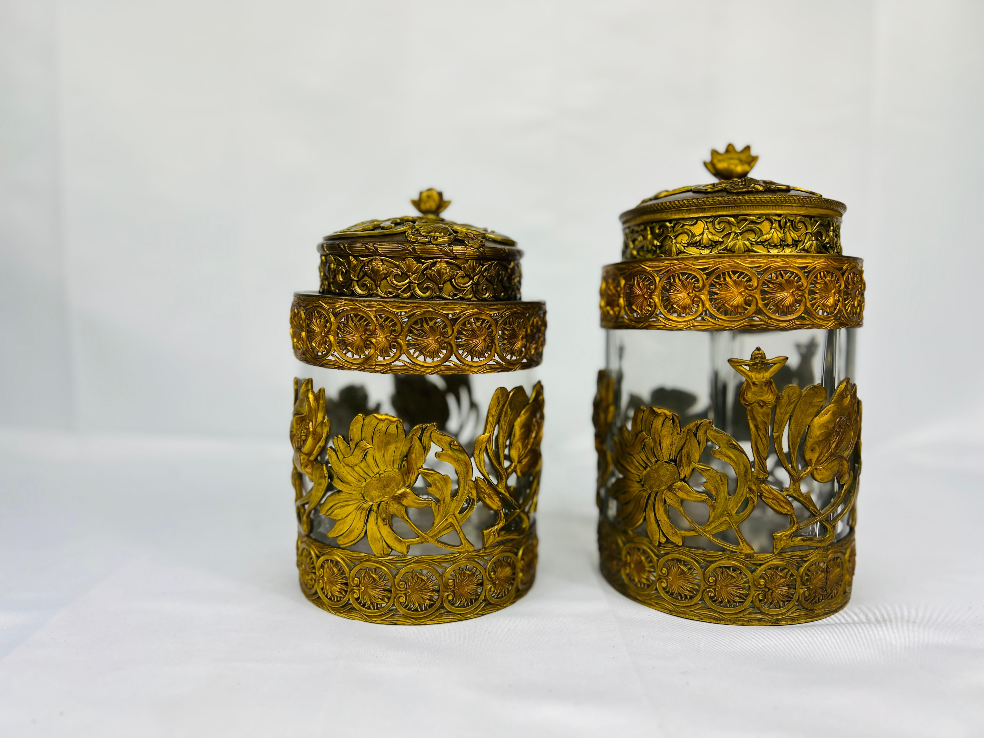 This exquisite antique liquor and humidor set combines delicate craftsmanship and functional elegance. Each piece is crafted from clear glass encased in gilded bronze filigree, showcasing intricate floral and foliate designs surrounding central