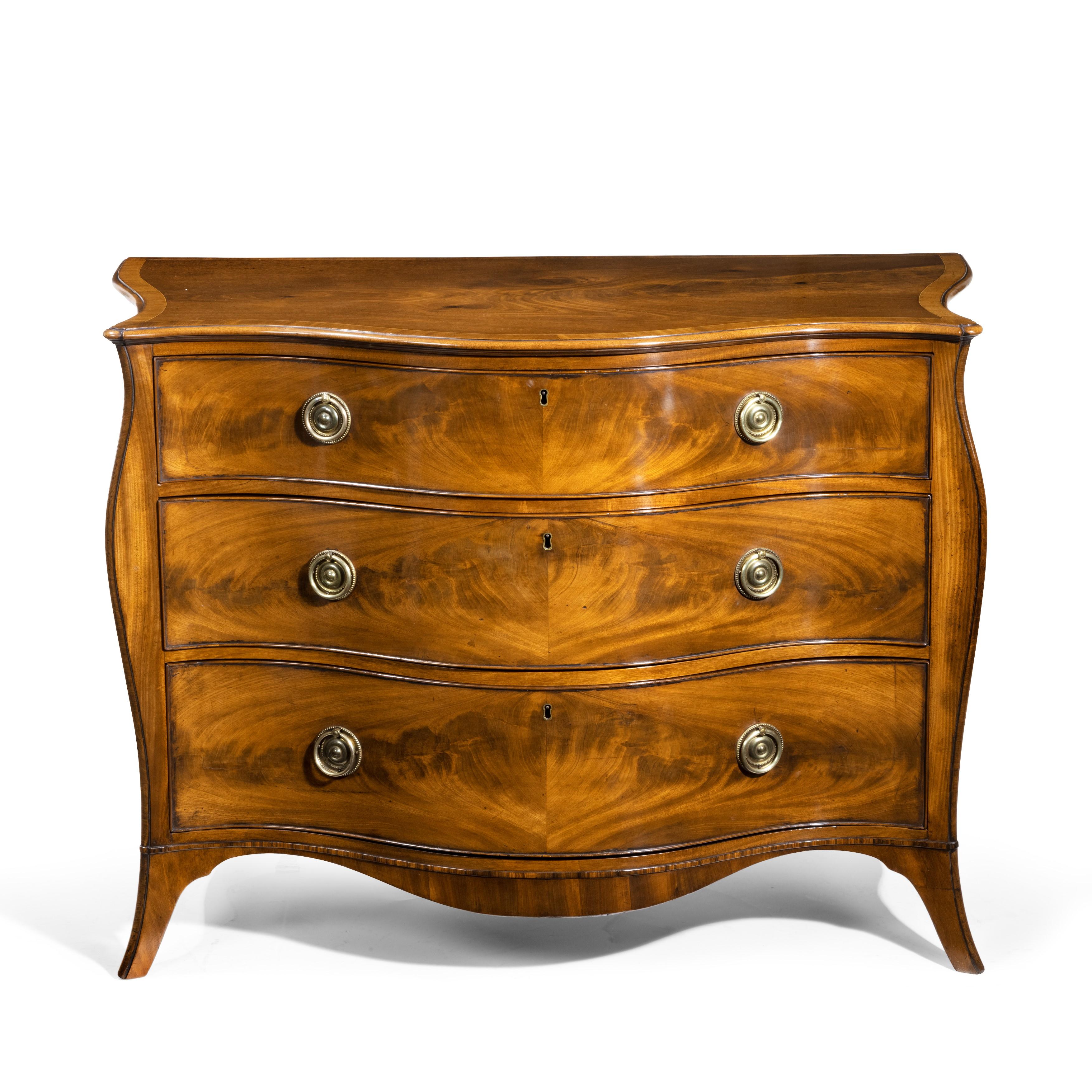 A fine George III figured mahogany serpentine commode attributed to Henry Hill of Marlborough, the serpentine top with a moulded edge above shaped sides and three graduated serpentine drawers fitted with the original gilt brass handles, bordered by