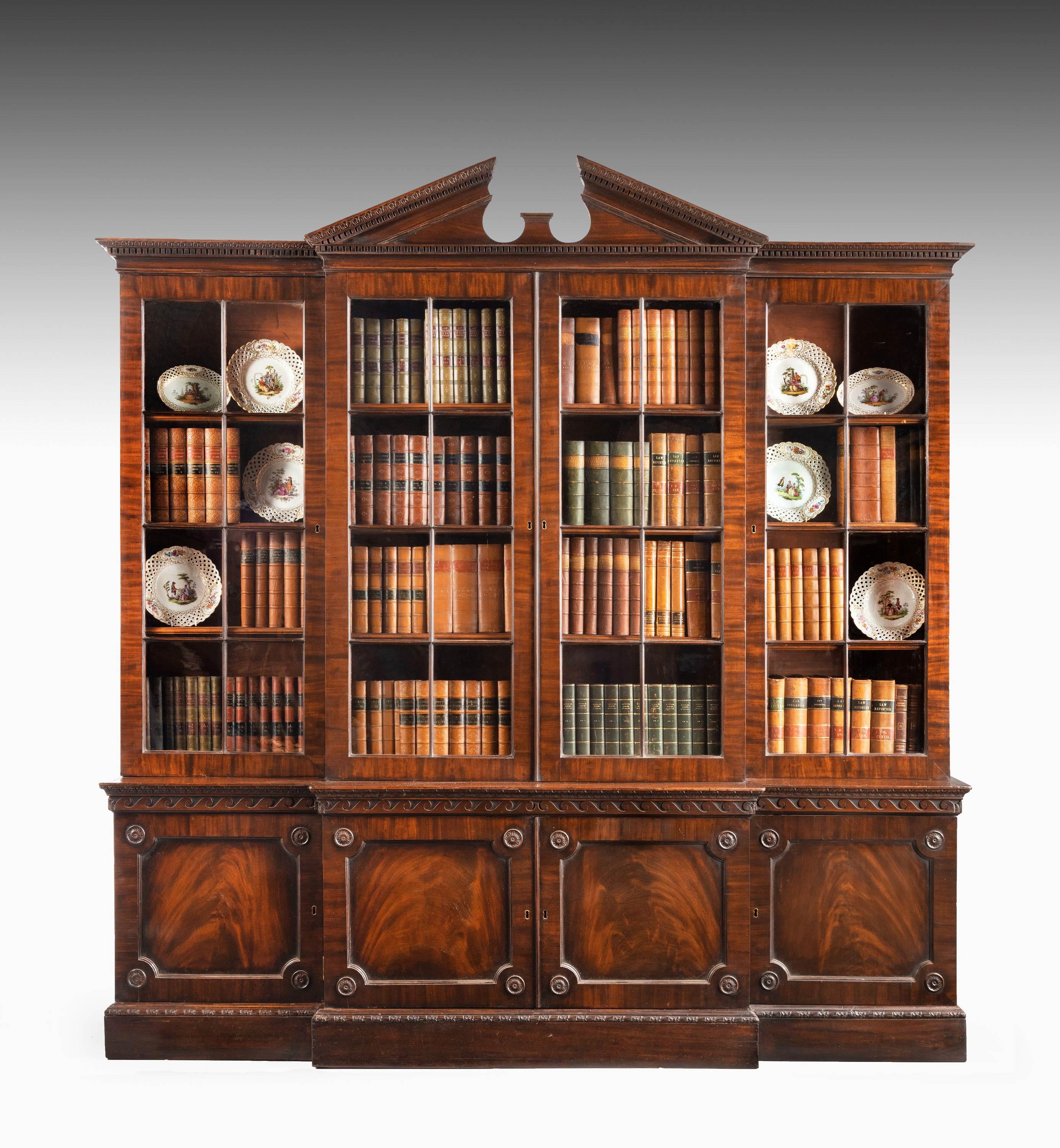 A particularly fine George III period mahogany breakfront bookcase of very good form. Low waisted and retaining the original broken arch pediment. With carved detail of the very best quality with the central waist bordered with Vitruvian scrolls and