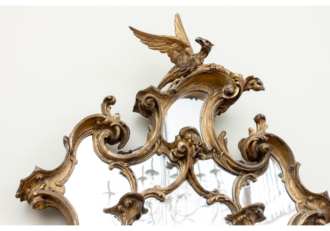 A striking and elaborate Georgian mirror with Bird Crest. English ca. later 18th c. A cartouche shaped mirror with scrolled foliate outside and inner surrounds. With a three-dimensional phoenix bird crest and small attached curved shelves on the