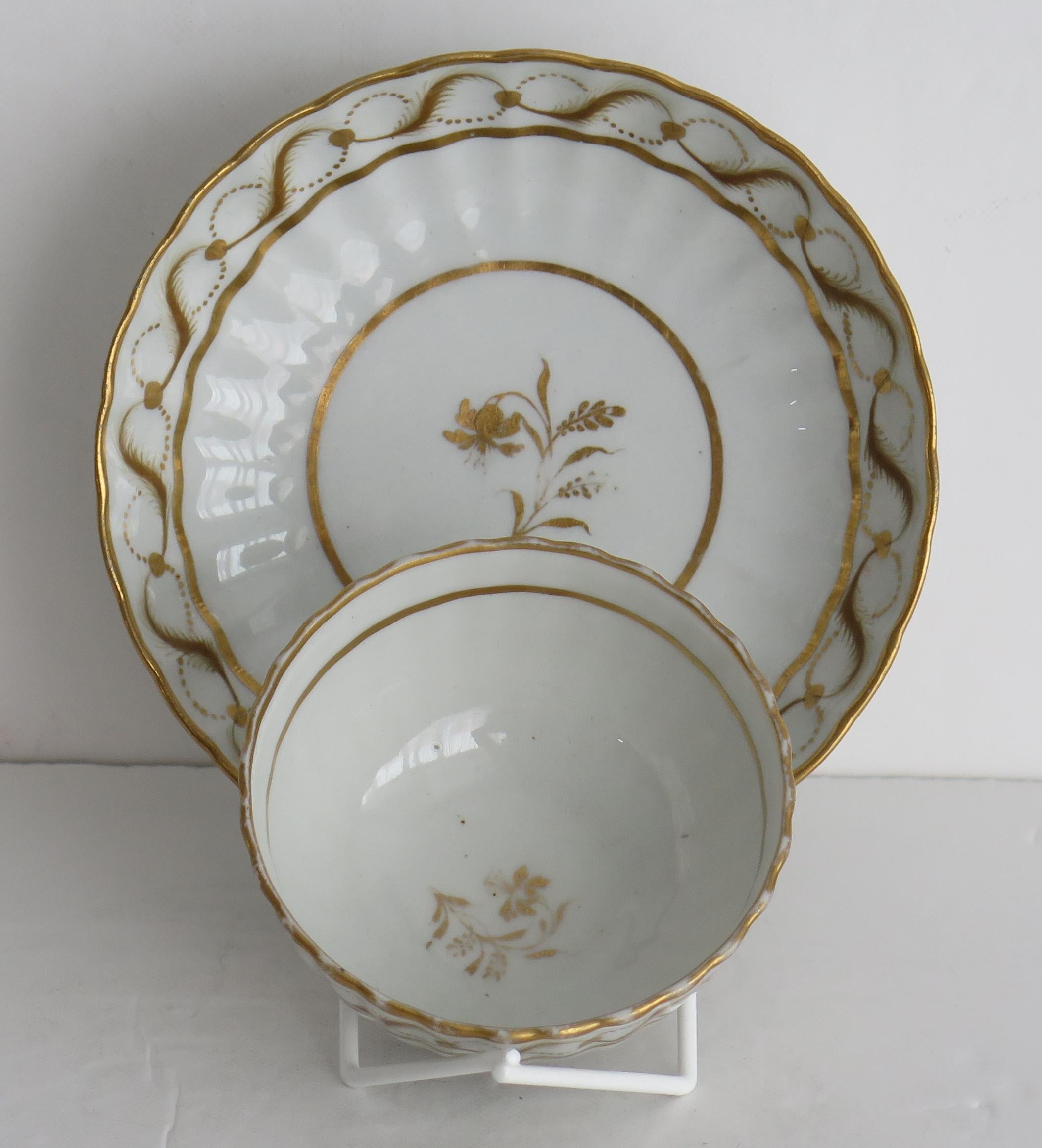 This is a very fine hard paste porcelain Tea Bowl and Saucer by New Hall, dating to the 18th century, George 111rd period, circa 1785.

Both pieces have 24 vertical flutes.

Both pieces are decorated over-glaze with a hand gilded gold painted