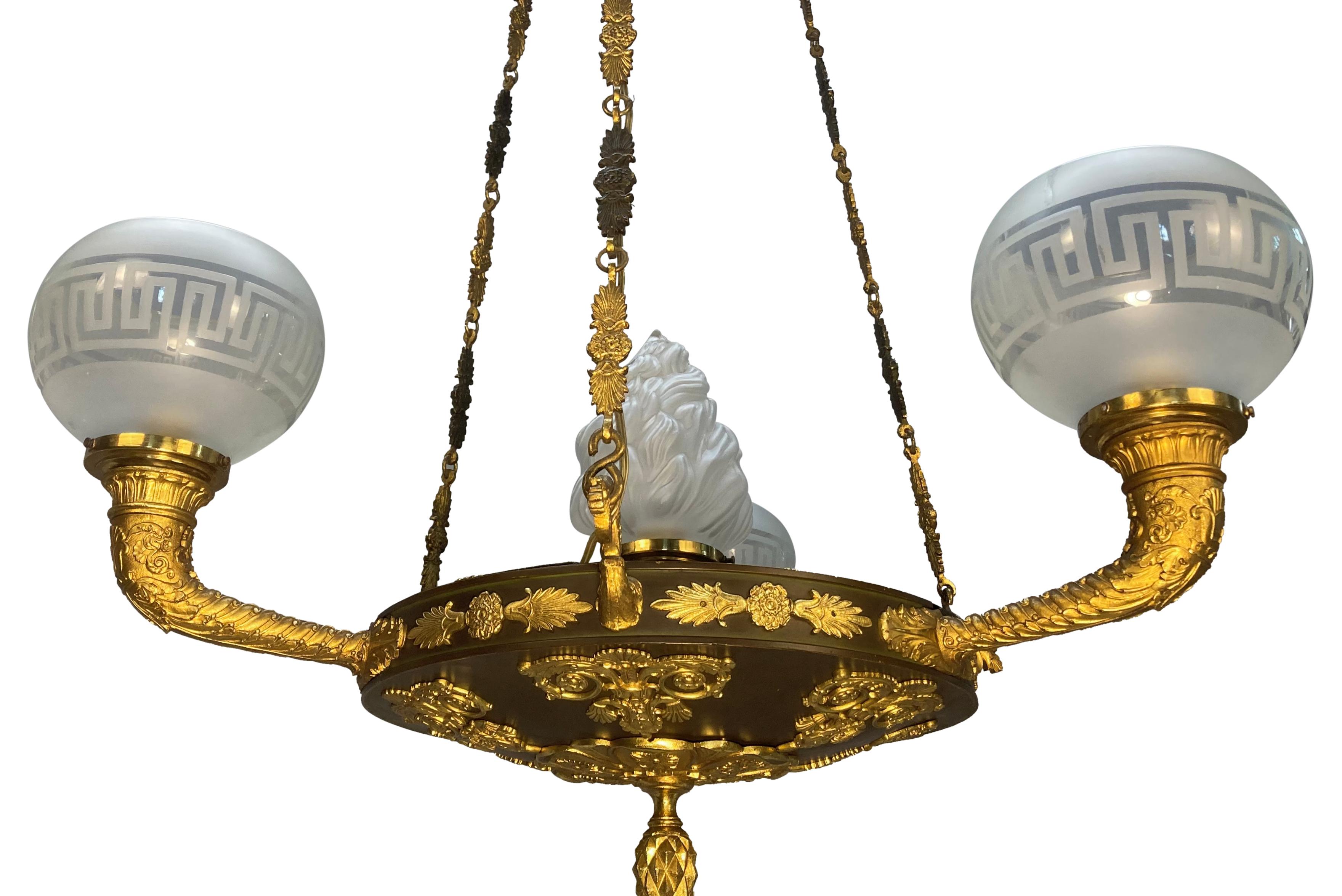 Eine feine Hängelampe im Regency-Stil aus vergoldeter Bronze und patiniertem Raps, mit fein gearbeiteten Akanthusdekorationen und Ketten. Mit vier Lichtern, drei davon mit Glasschirmen mit griechischem Schlüssel und einer zentralen Glasflamme.