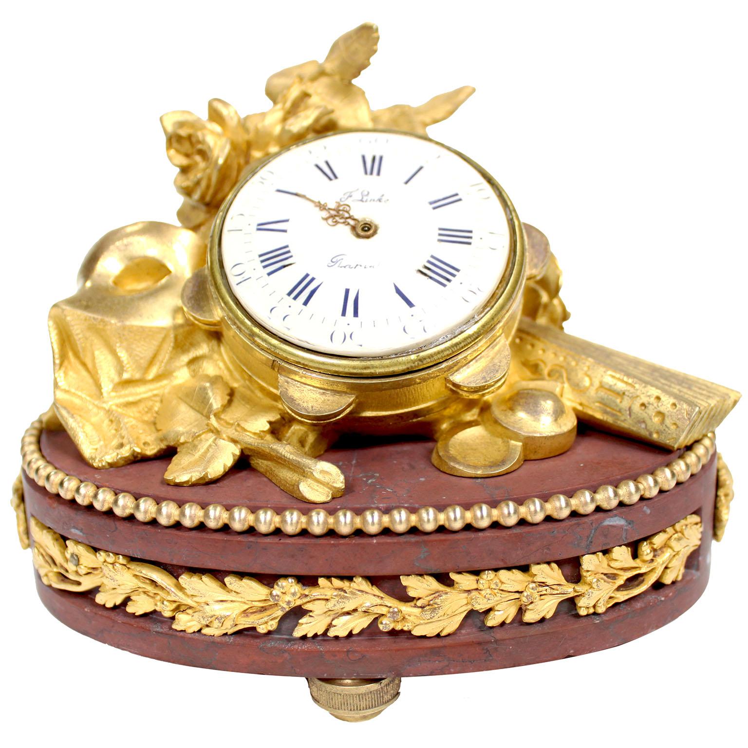 Pendule de table en bronze doré et marbre rouge griotte de François Linke (1855-1946) du XIXe siècle. Numéro d'index 86. Le boîtier de la pendule est orné d'un tambourin au milieu de roses en fleurs, d'un masque et d'un éventail, sur un socle ovale
