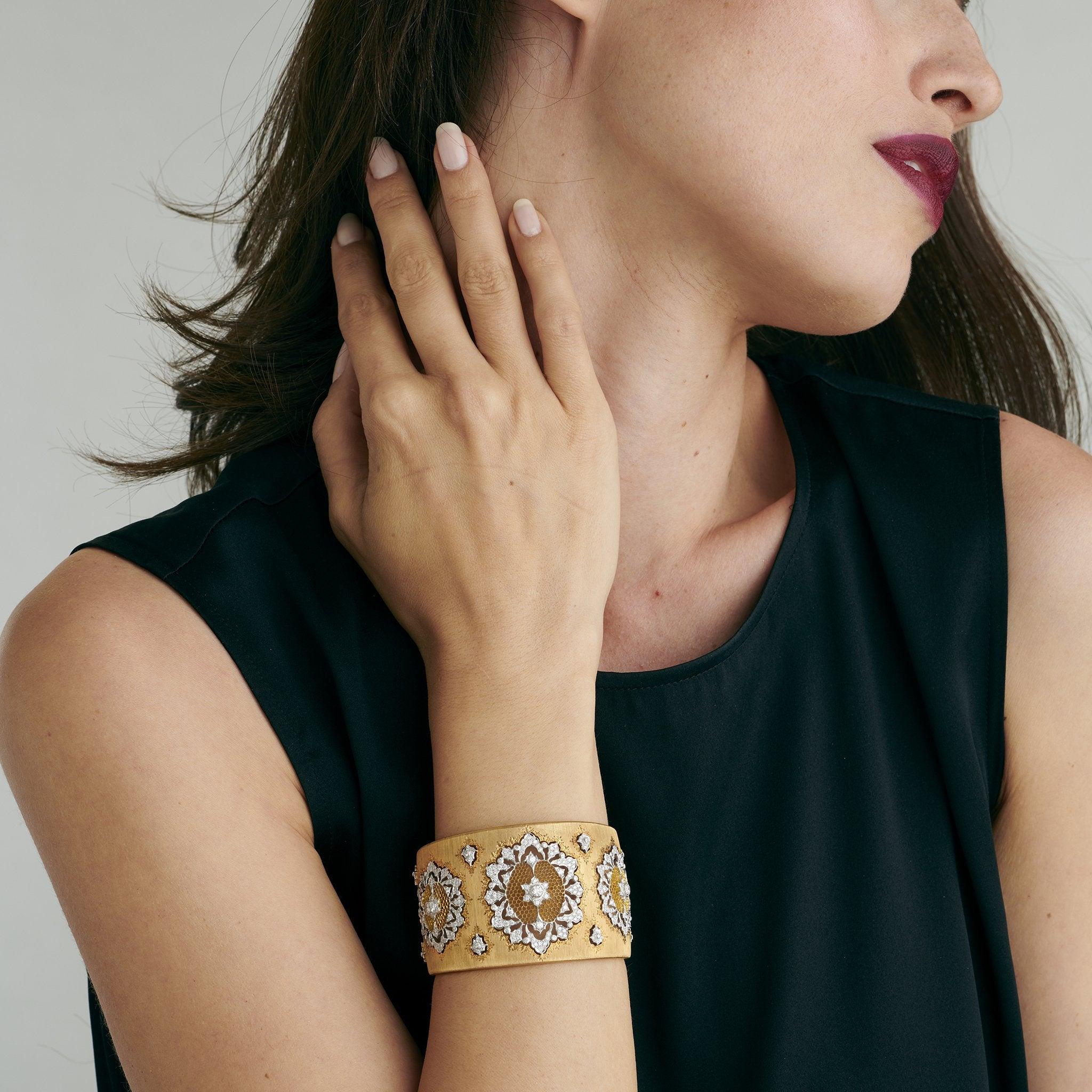 Dieses opulente Manschettenarmband aus zweifarbigem Gold und Diamanten ist ein Entwurf von Buccellati. Die leicht spitz zulaufende Manschette mit vertikal gerillter Oberfläche ist mit drei durchbrochenen, spitzenähnlichen Blumenmotiven aus Weißgold