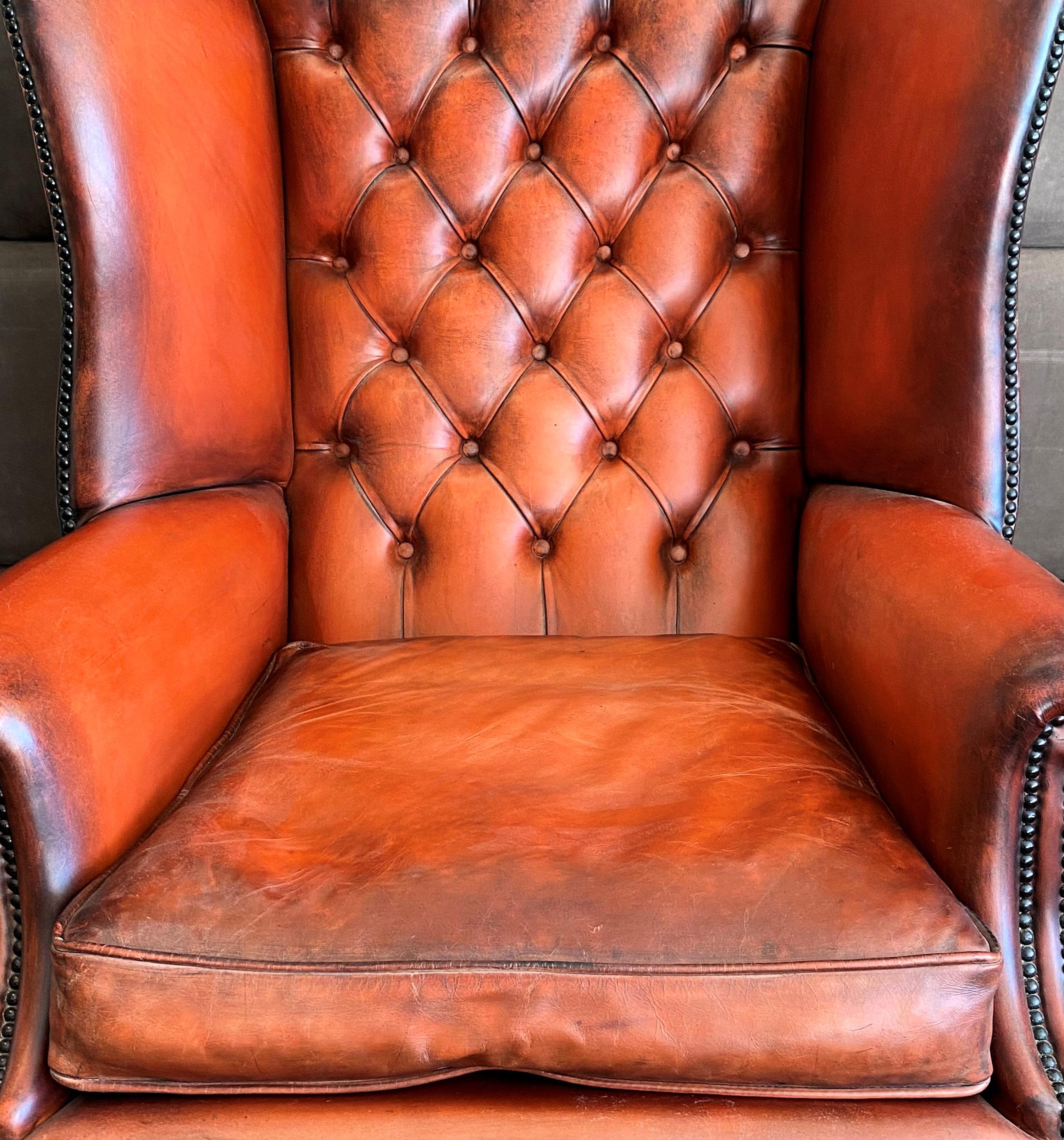 This fine quality and very handsome handmade English leather wing armchair features a ball and claw leg in the 18th century style. It has a button back and separate cushion seat made to the traditional standard. The leather is naturally worn to a