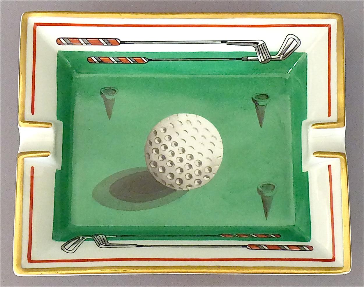A fine and beautiful Hermès Limoges vintage oblong porcelain ashtray with golf ball motif in Fornasetti style, partly gilt, in colors green, white, grey and red. Marked Hermes Paris and Made in France to the side and suede covered to the base for