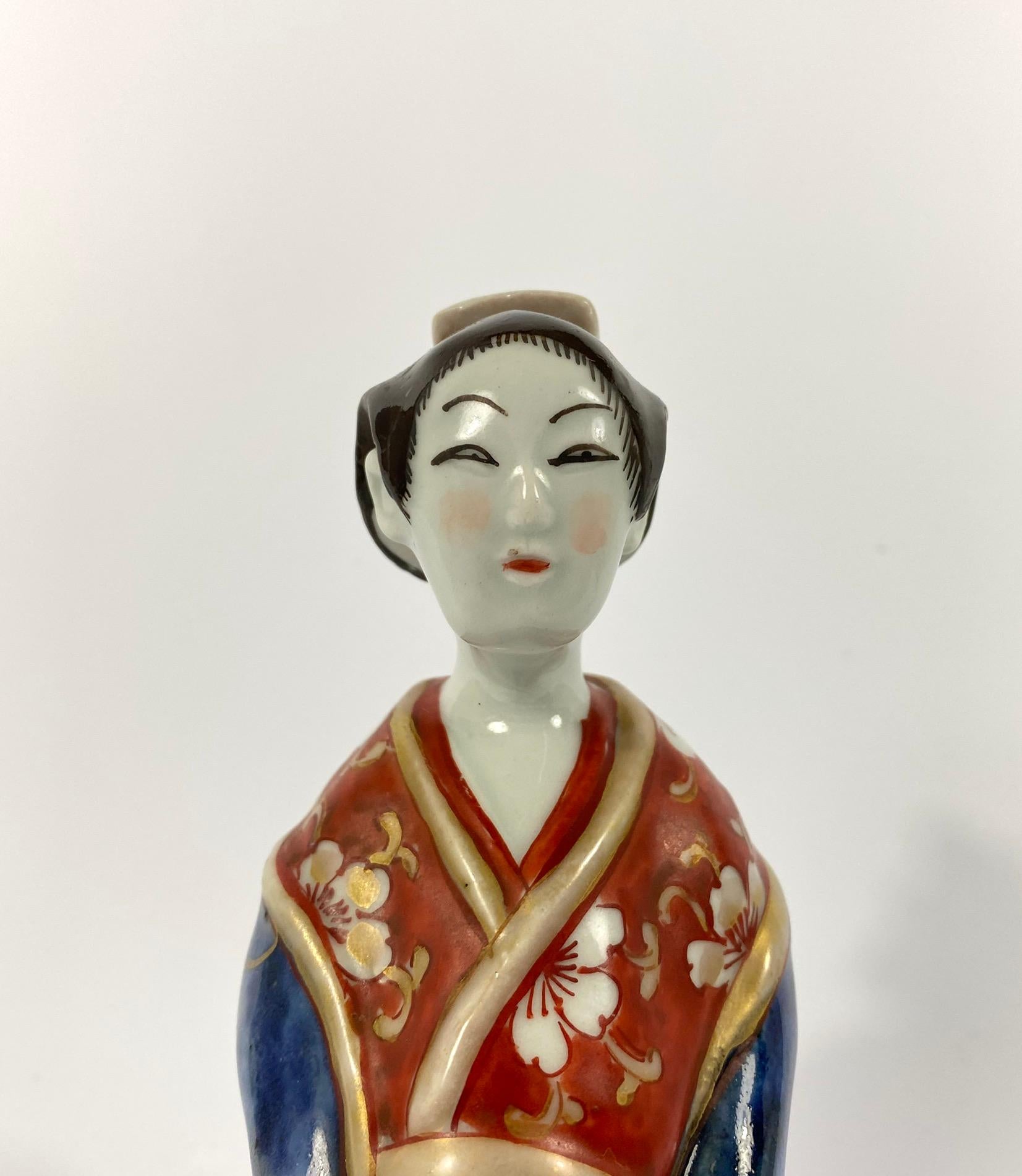 A Japanese Imari porcelain figure, circa 1700, Genroku Period. Finely modelled as a Bijin, wearing an elaborate underglaze blue kimono, painted with large flowerheads, on an iron red ground, and heightened with gilt flowering plants.
Having an