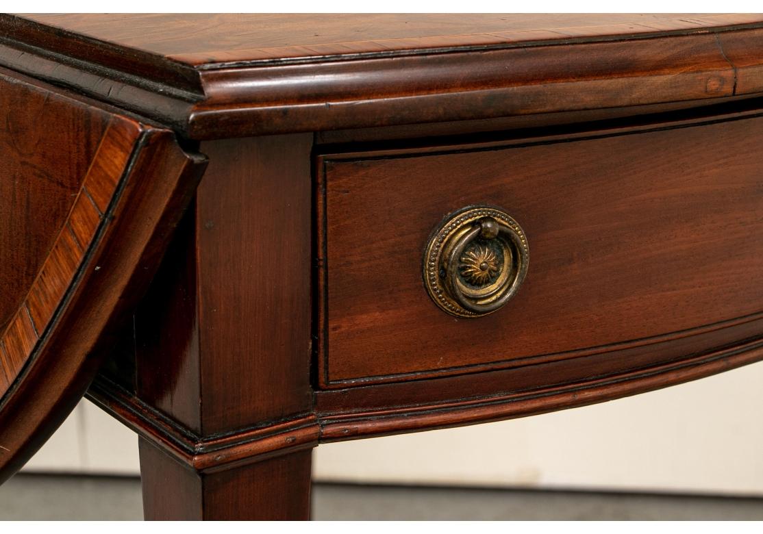 A very well made Pembroke with a highly decorative and colorful mix of woods. With a cross banded top and leaves in a stained pattern, and a fine inlaid fan in the center. A drawer on each end (lacking a key). Finely cast brass pulls. 
L. 29