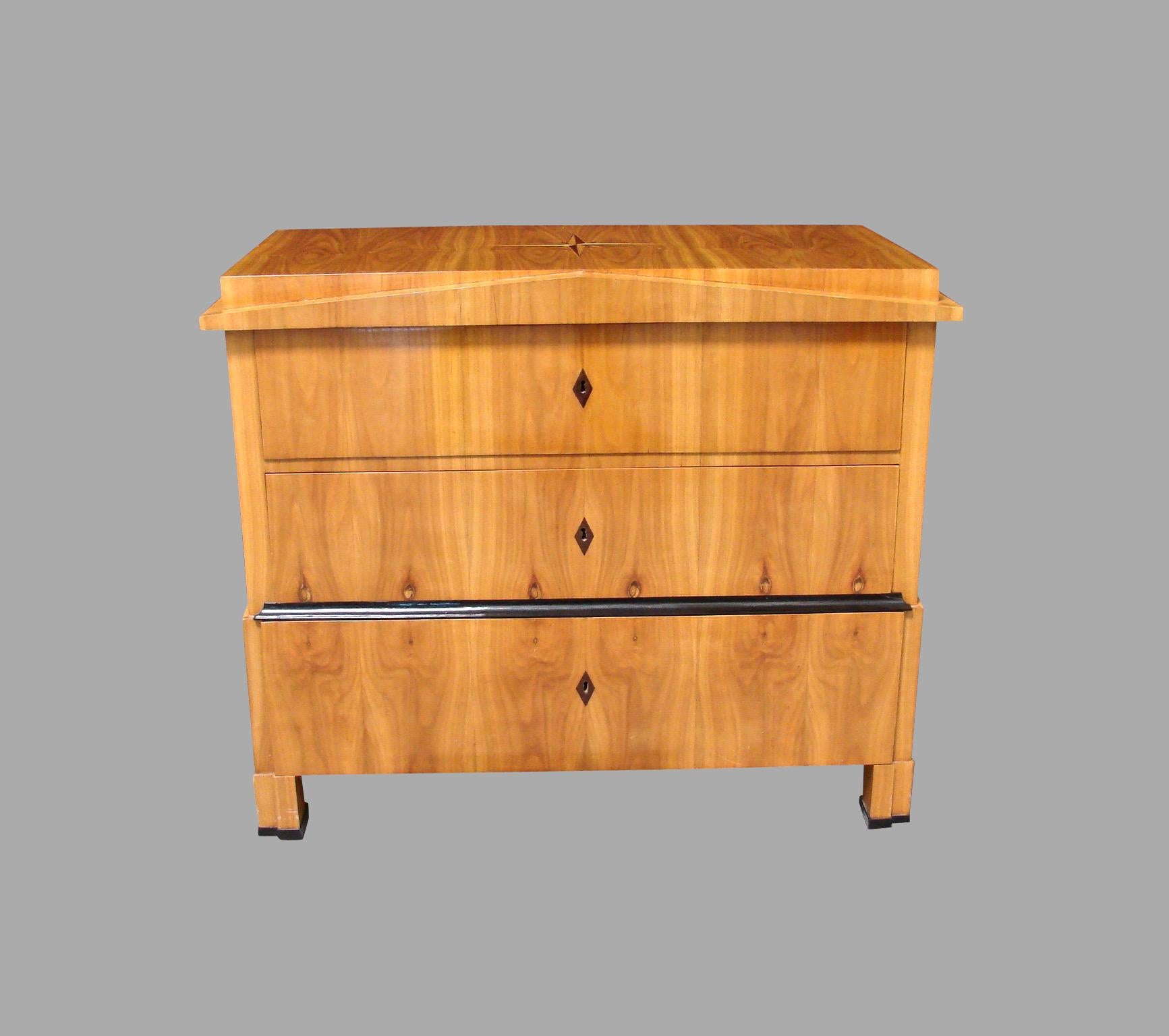 A fine inlaid Austrian pearwood or fruitwood Biedermeier commode of architectural form, the top inlaid with a compass star, the front with a triangular pediment above 3 long drawers with ebonized keyhole escutcheons supported on block feet with