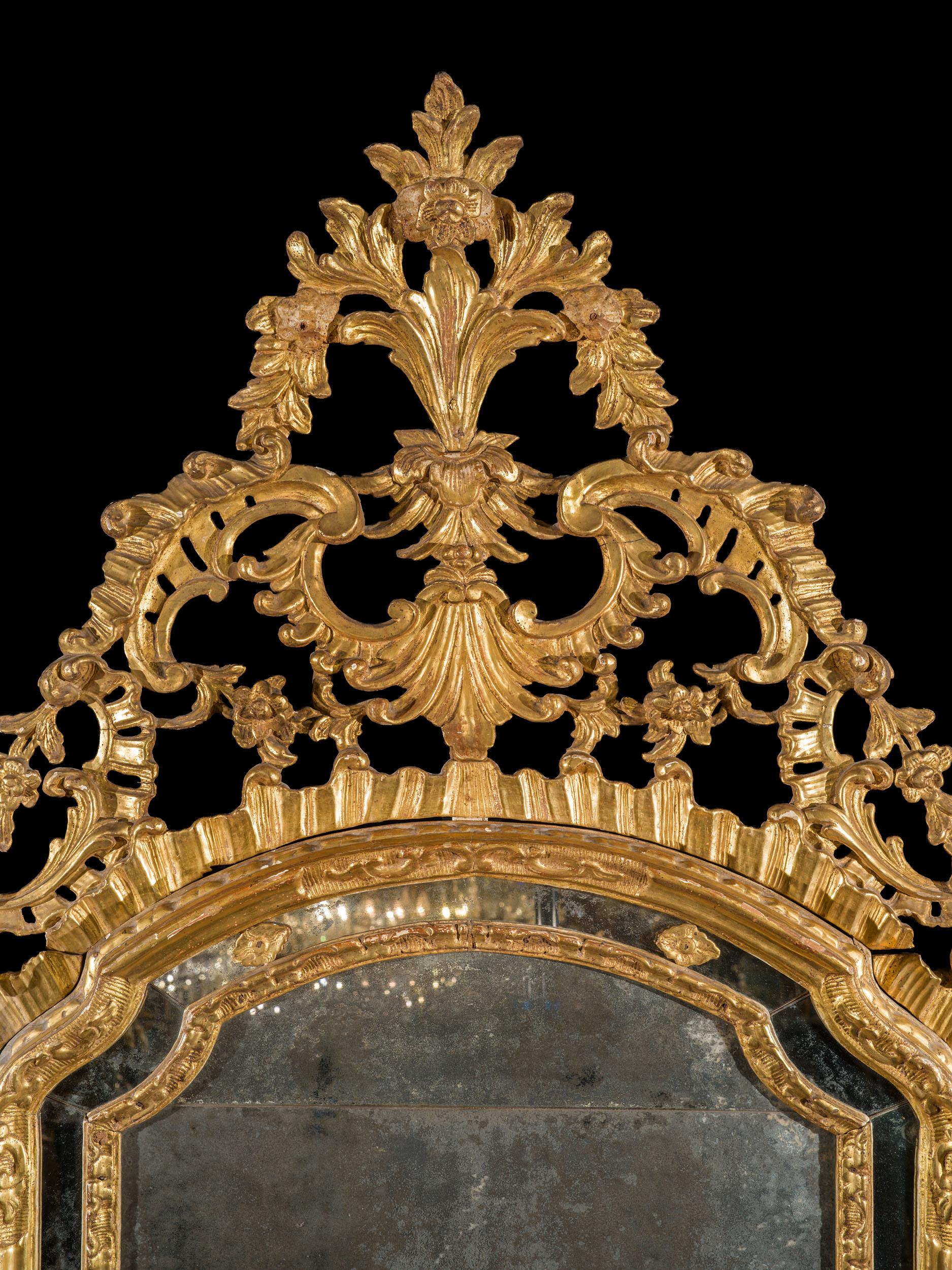 Très beau miroir piémontais en bois doré. Ce magnifique miroir possède une plaque de mercure arquée et merveilleusement patinée, entourée d'une fine plaque marginale du même verre. Le cadre raffiné en rocaille est surmonté d'une magnifique crête en