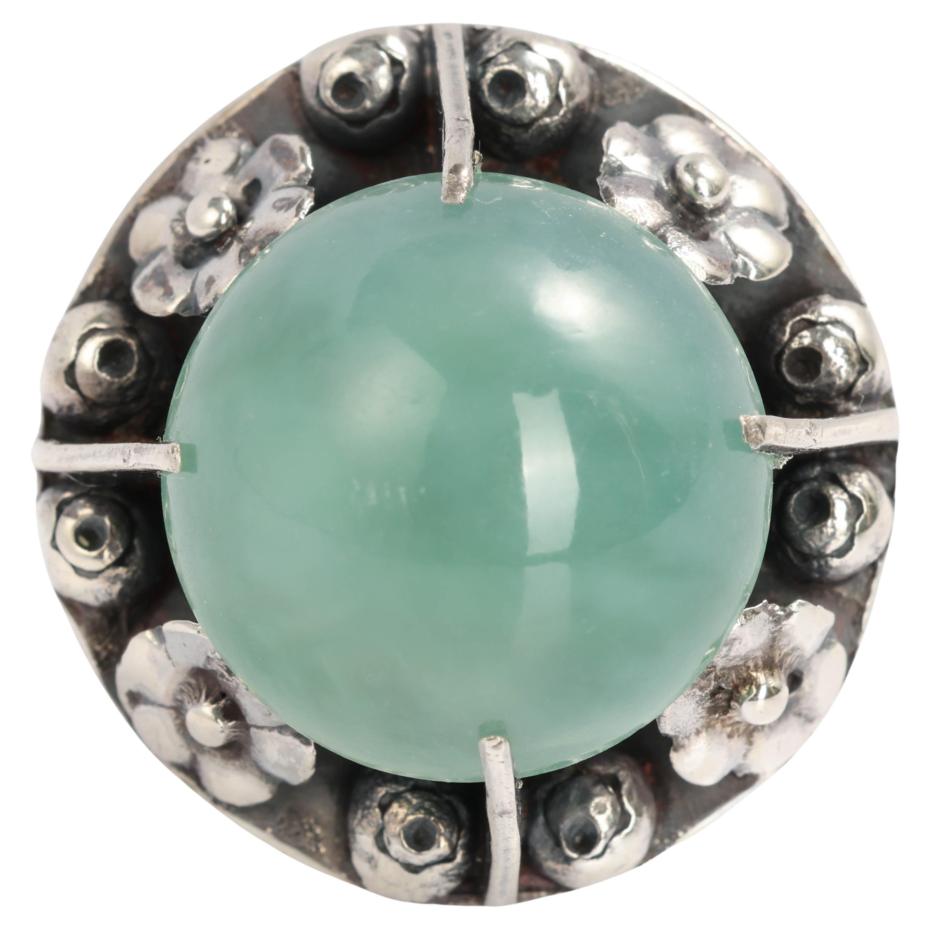 A huge, light seafoam-green cabochon of semi-transparent, natural, and untreated Burmese jadeite jade glows from across the room in its handmade silver Arts & Crafts era mounting.  I have seen similar 