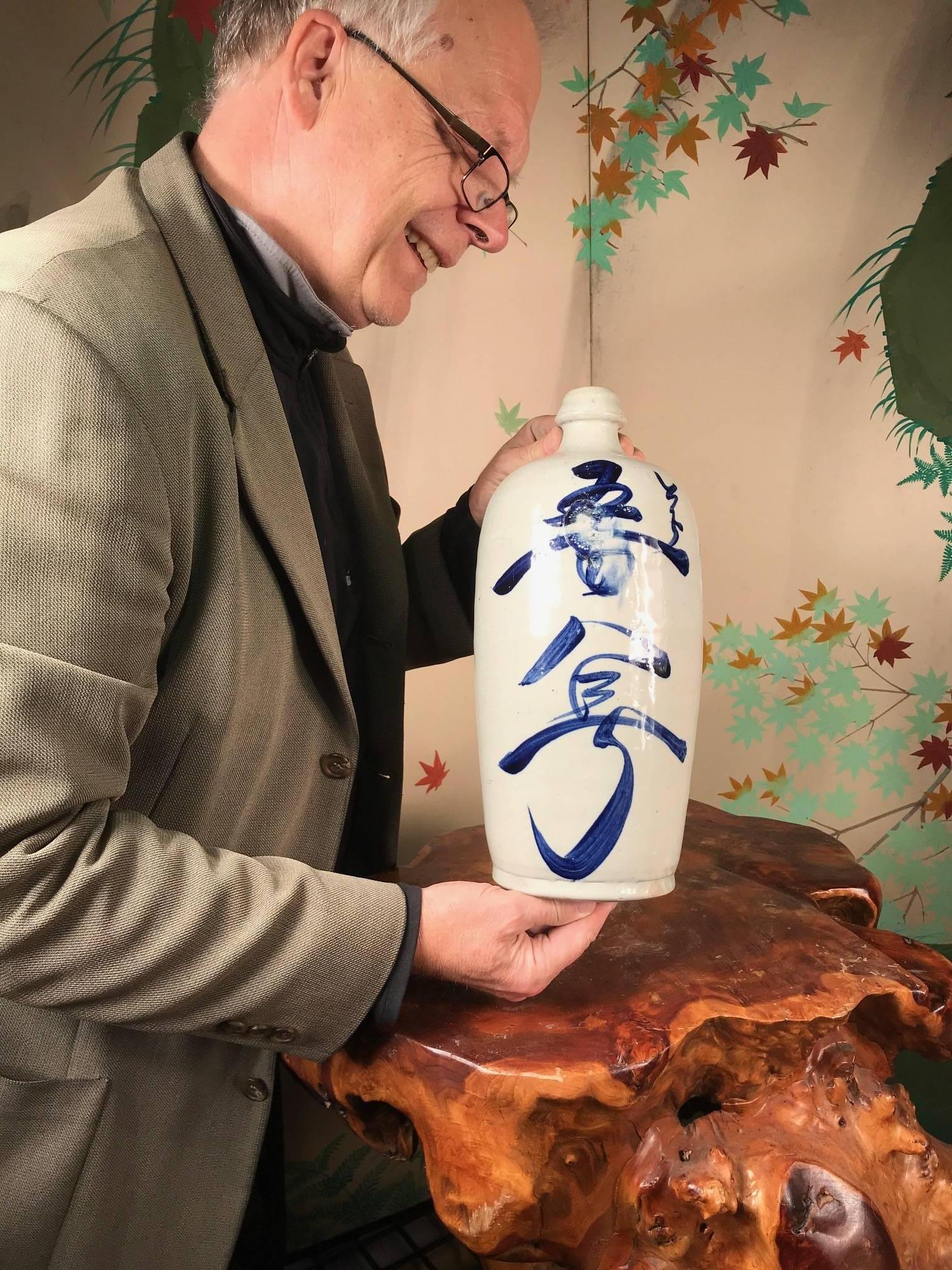 Here's a wonderful example of a fine antique Japanese hand-painted tall ceramic sake bottle. Notice the superb calligraphy detailed in cobalt blue glaze- trademarks of exquisite Japanese artistry. Calligraphy details the maker and brand.

This is a