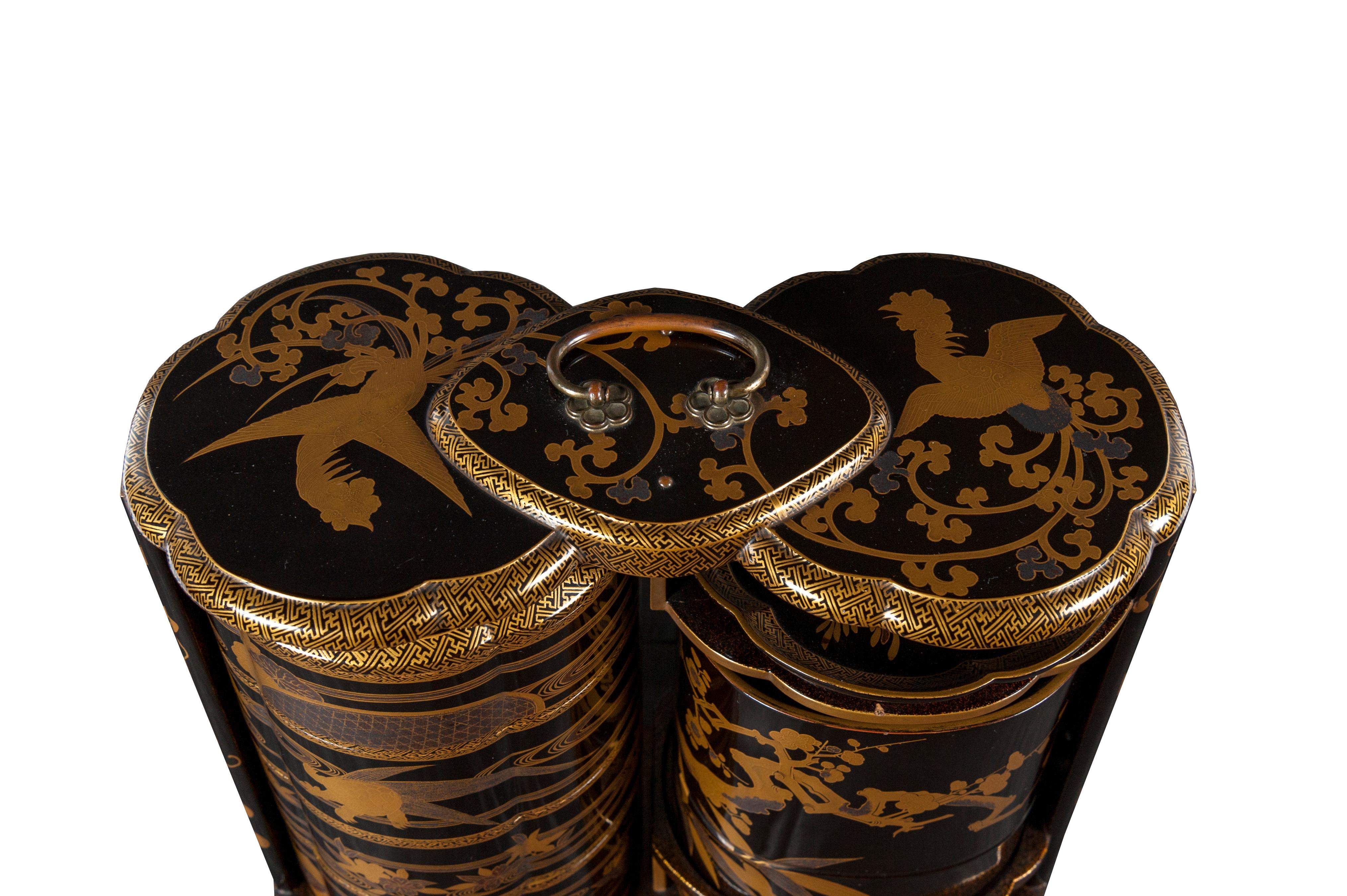 Black and gold lacquer sageju-bako (picnic box) decorated with floral motifs in hiramaki-e. It includes a sake bottle, a four-compartment box with nashi-ji lacquer inside, a simple tray and a hollow tray. At the top, there is a bronze handle for