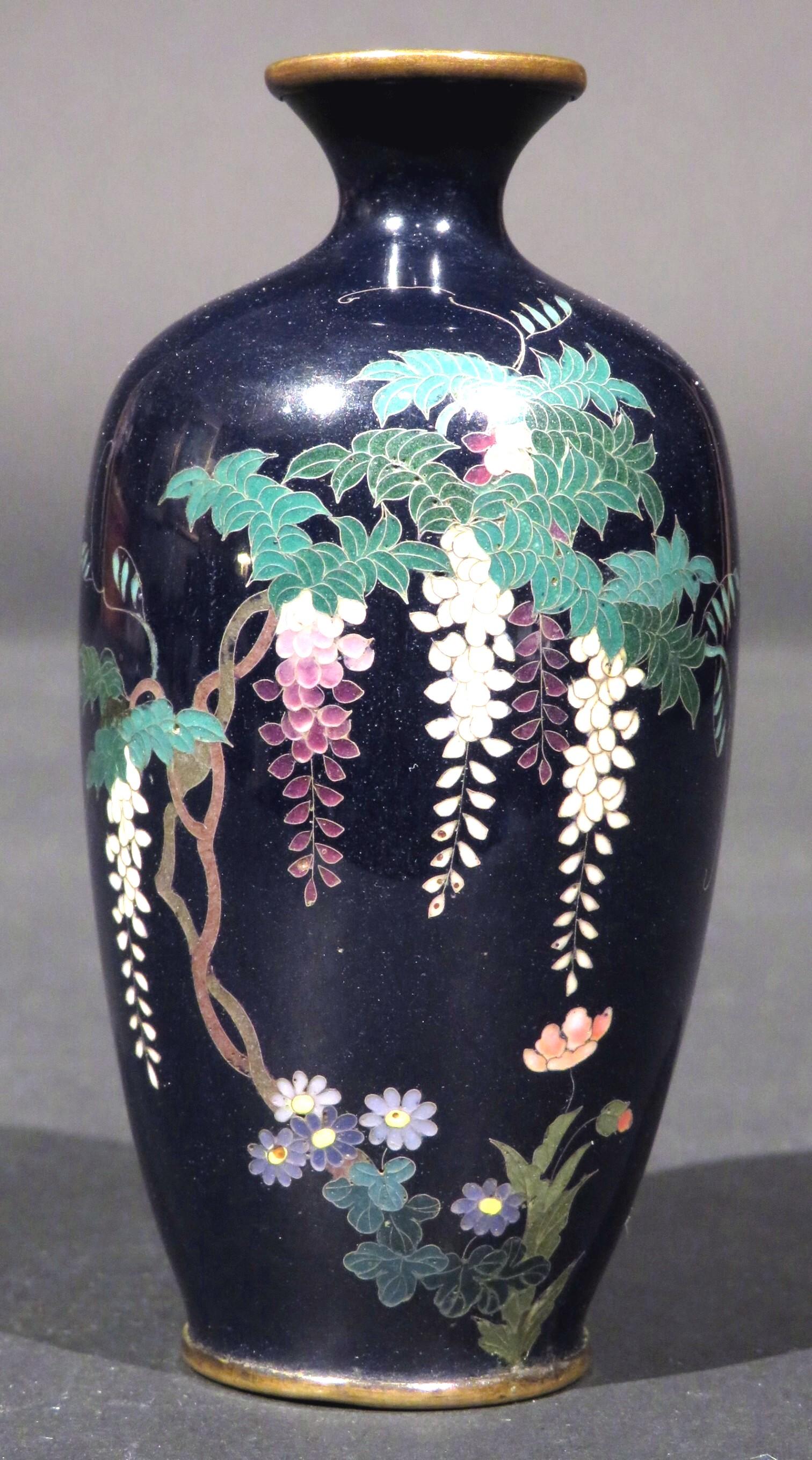 The baluster shaped body rising to a flaring neck & rim, richly decorated with flowering boughs of wisteria & exotic flora finely worked in silver wire and enamels, set against an indigo blue ground.
 