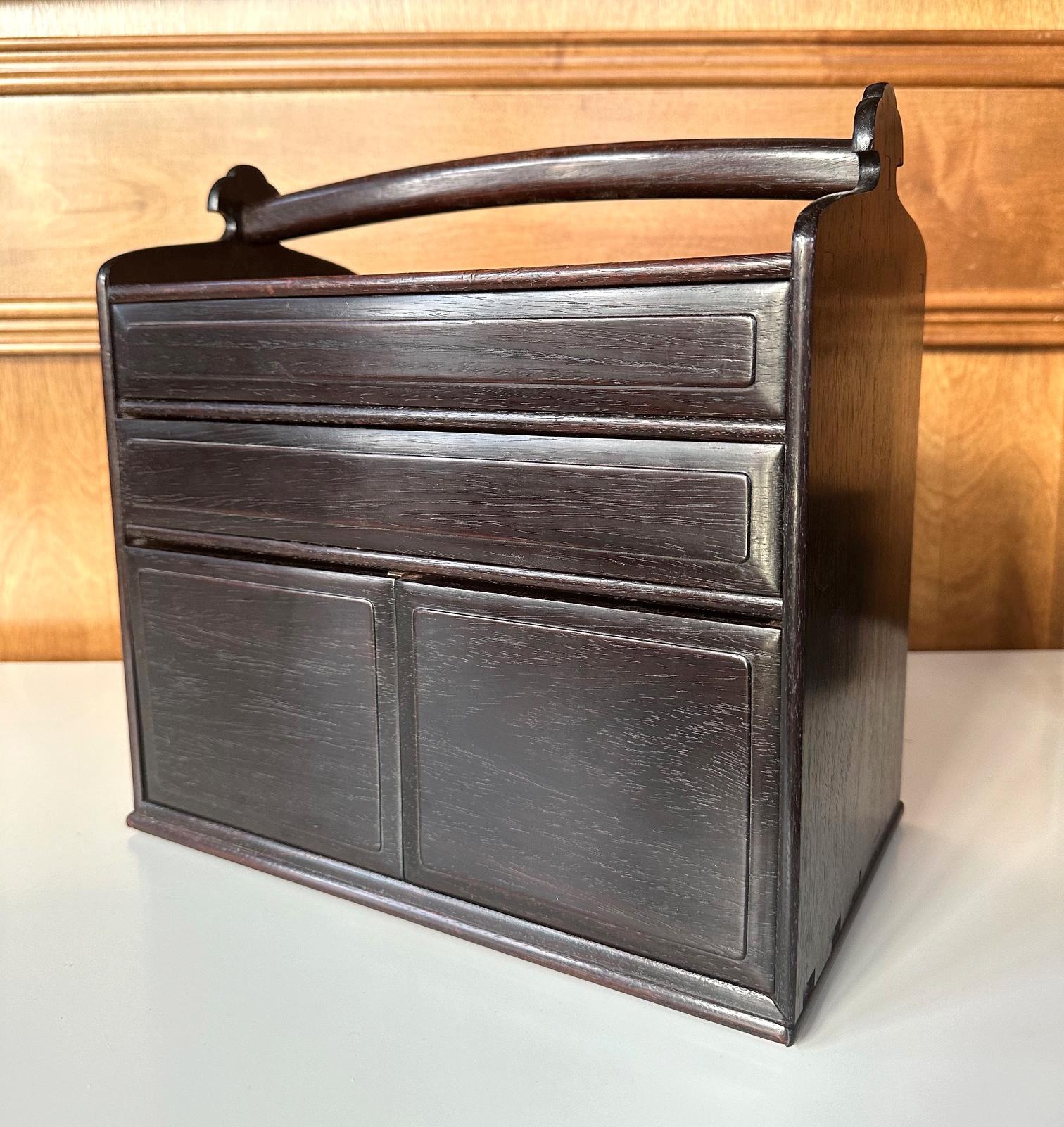 An antique Japanese portable cabinet finely fashioned out of Sandalwood, a fragrant and also one of the most expensive woods that was used to make small luxury pieces. The handled cabinet was stained in a deep reddish color and has a very modern