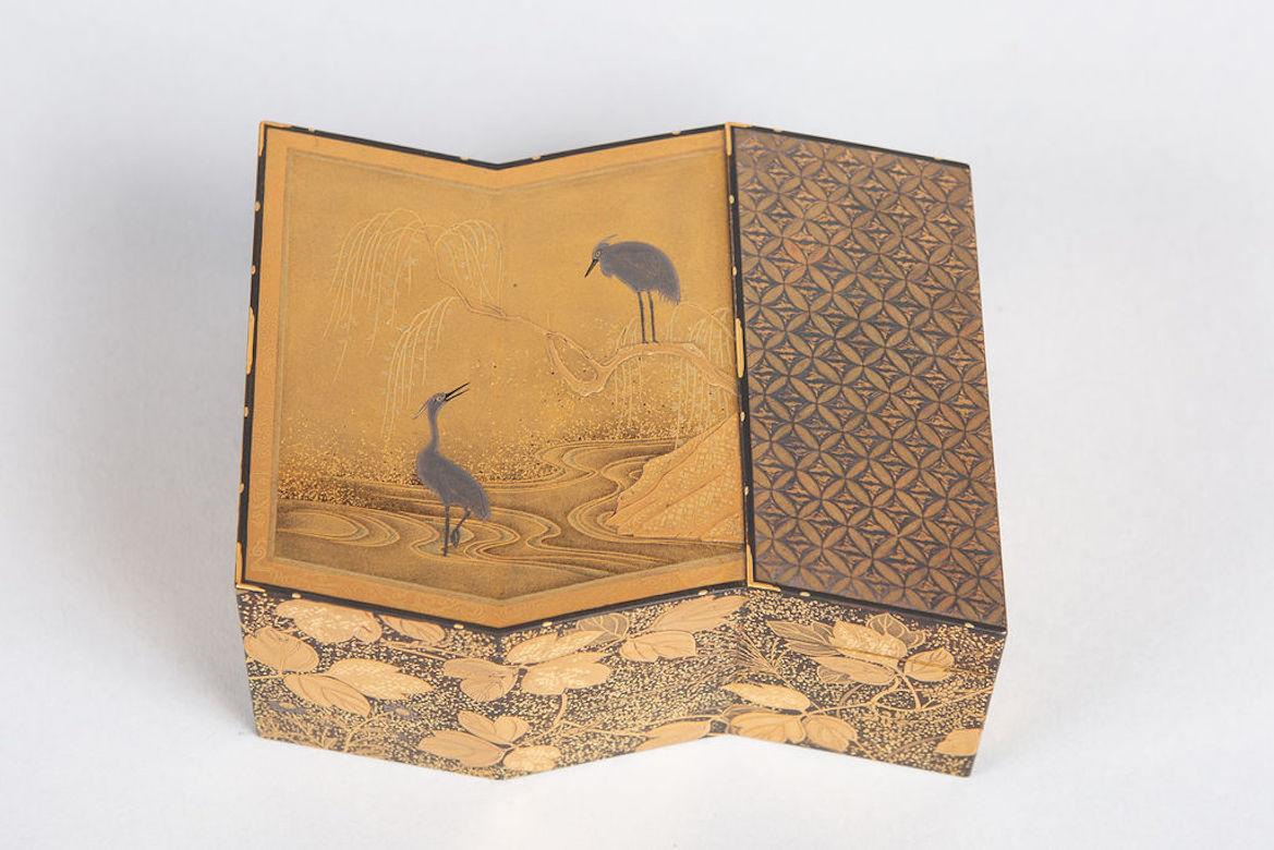 Exquisitely detailed incense storage box in gold lacquer with silver and gold overlays of a folded screen with heron and willow design. Flowers and winding leaves on the sides.