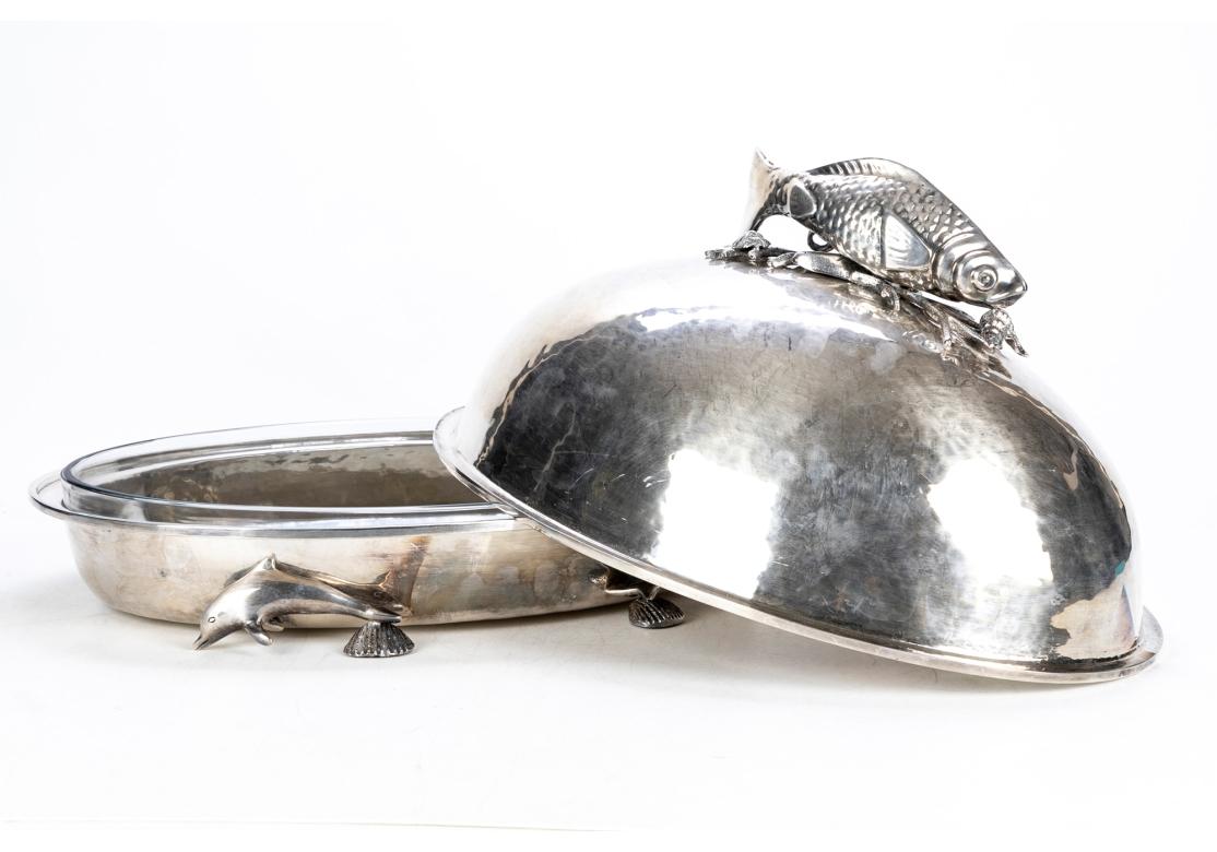 Un grande server ovale in argento martellato con un alto piano a cupola con un grande pesce ben fuso con conchiglie, motivi di corallo e un cavalluccio marino come manico. Sollevato su quattro piedi a forma di delfino con conchiglie. Viene fornito