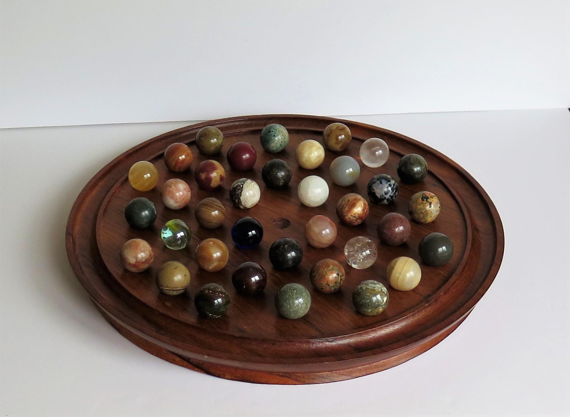 This is a very decorative and complete board game of 37 hole marble solitaire with a very large 13.5 inch diameter hardwood board and 36 beautiful individual mainly agate stone and some glass marbles, which we date to the late 19th-early 20th