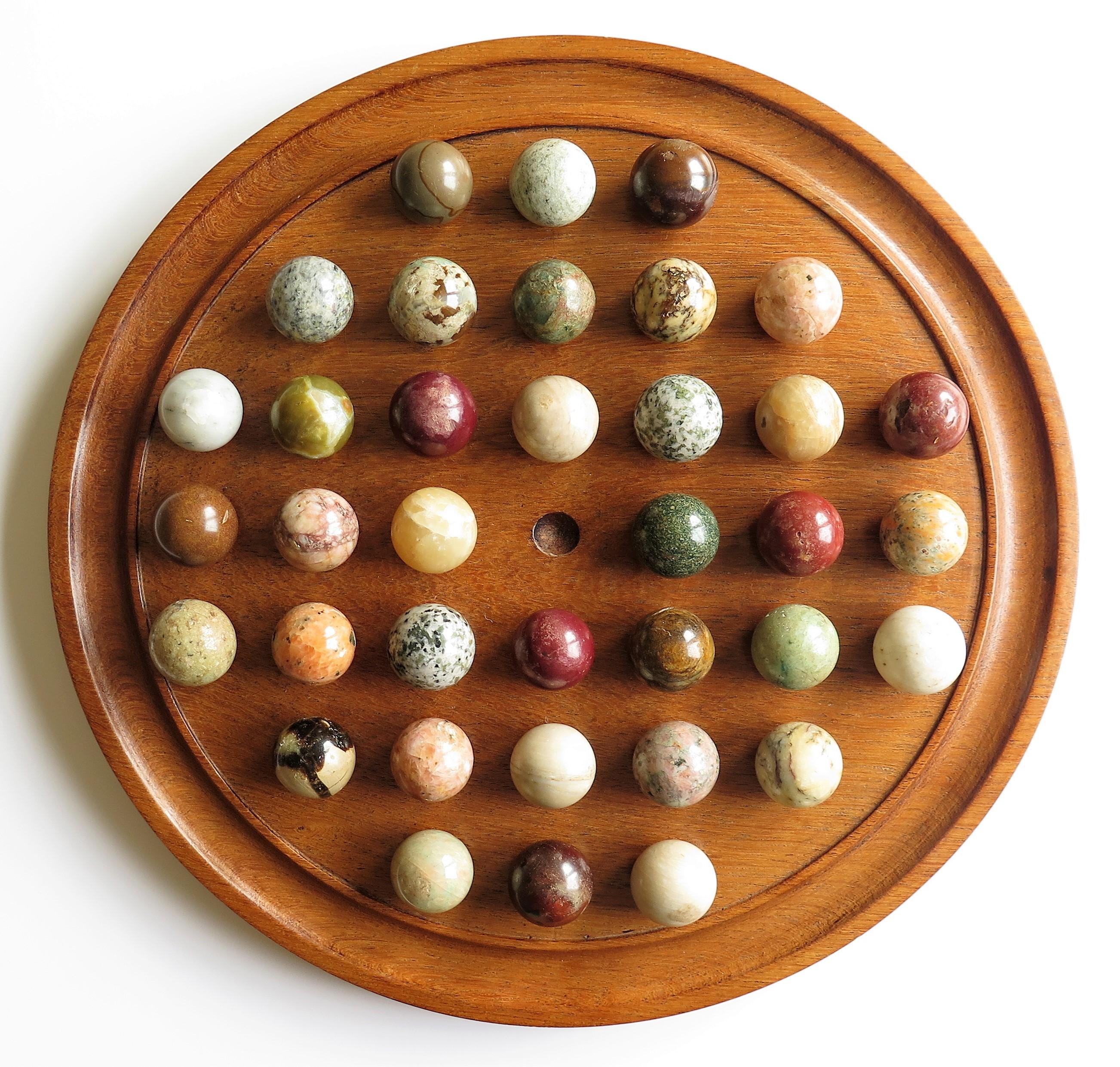 This is a very decorative and complete board game of 37 hole marble solitaire with a very large 14.5 inch diameter hardwood board and 36 beautiful individual agate stone marbles, which we date to the late 19th century, probably of French