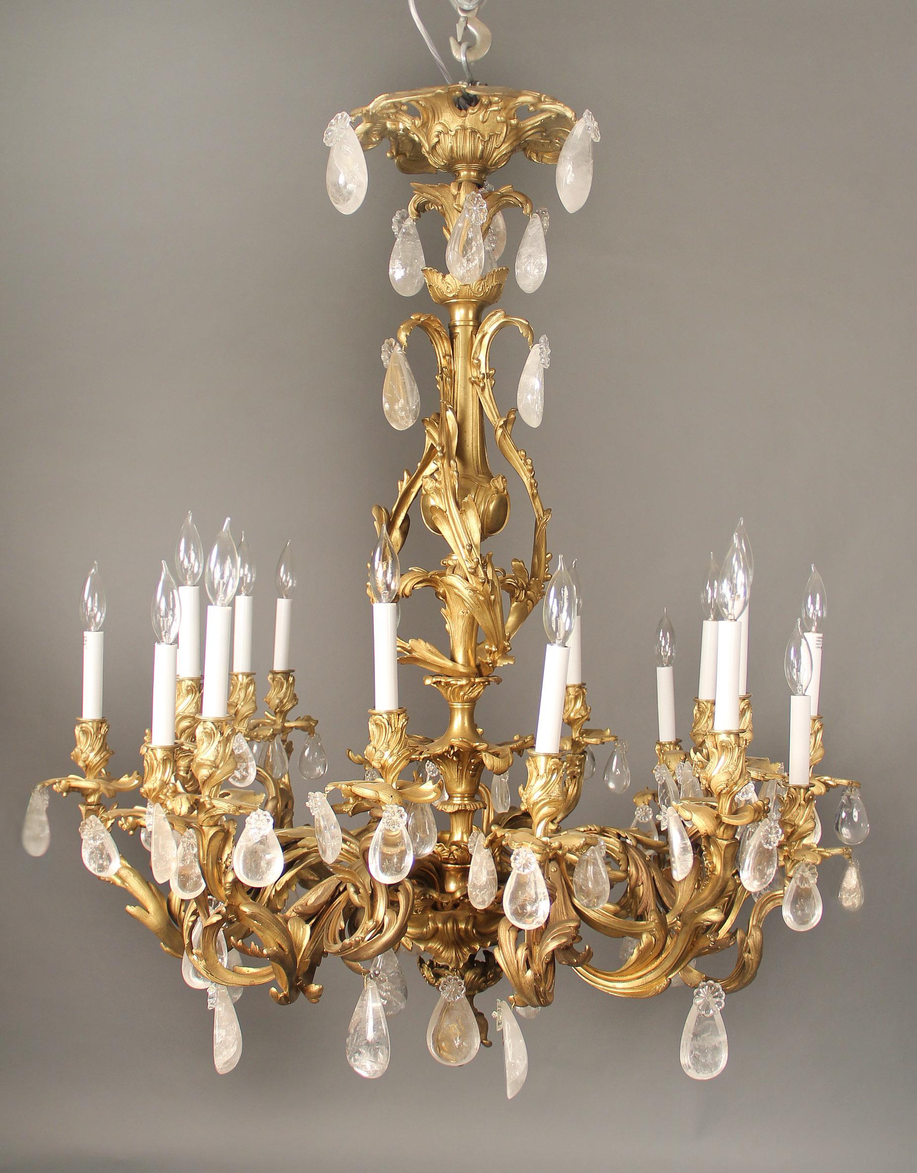 A fine late 19th century gilt bronze and rock crystal eighteen light chandelier

Tear shaped rock crystal, heavy bronze foliage designed arms, the central column with a large urn and the base ending with a floral acorn, eighteen perimeter lights.