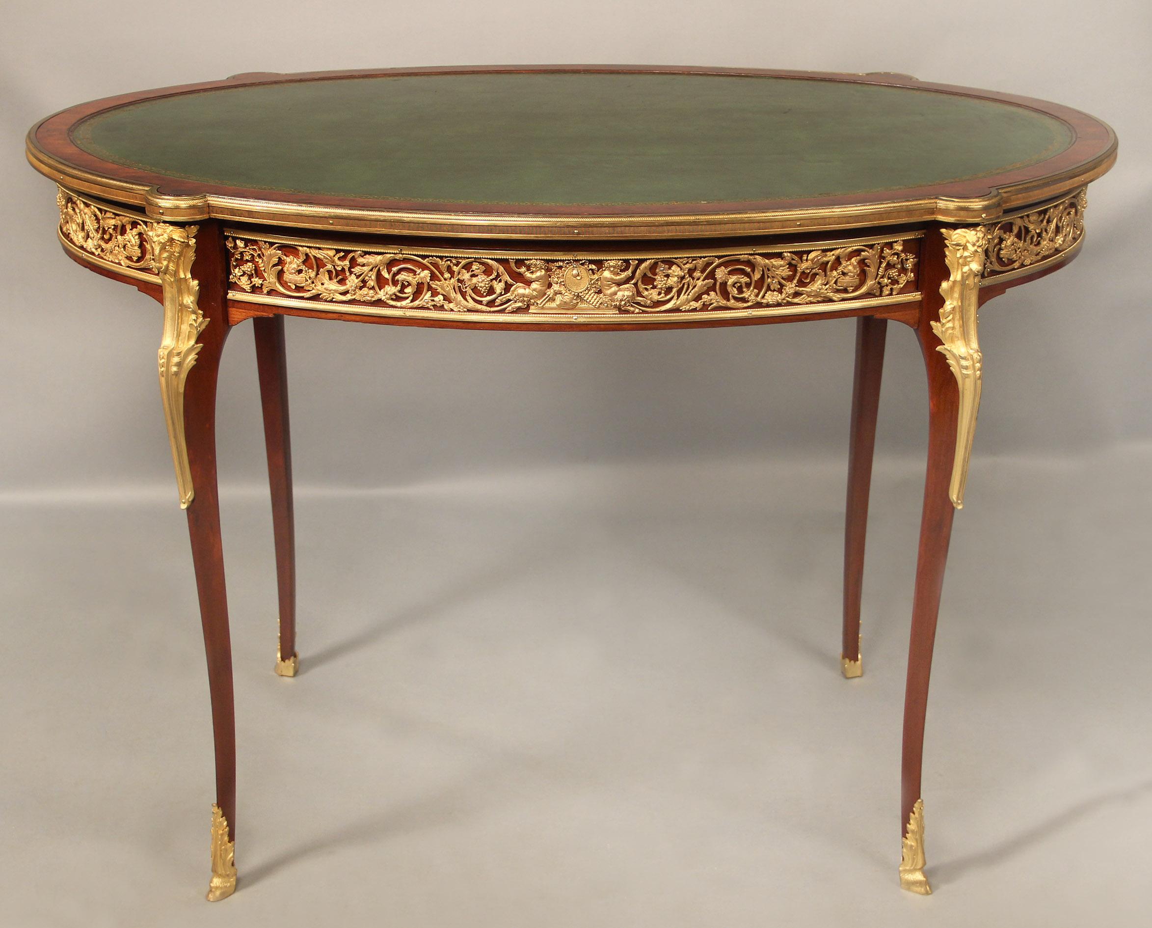 A fine late 19th century gilt bronze-mounted Louis XV style table

The shaped oval leather top with a molded border, above a foliated frieze centered to the front and back by satyrs and musical trophies, the front opening as a drawer, on four