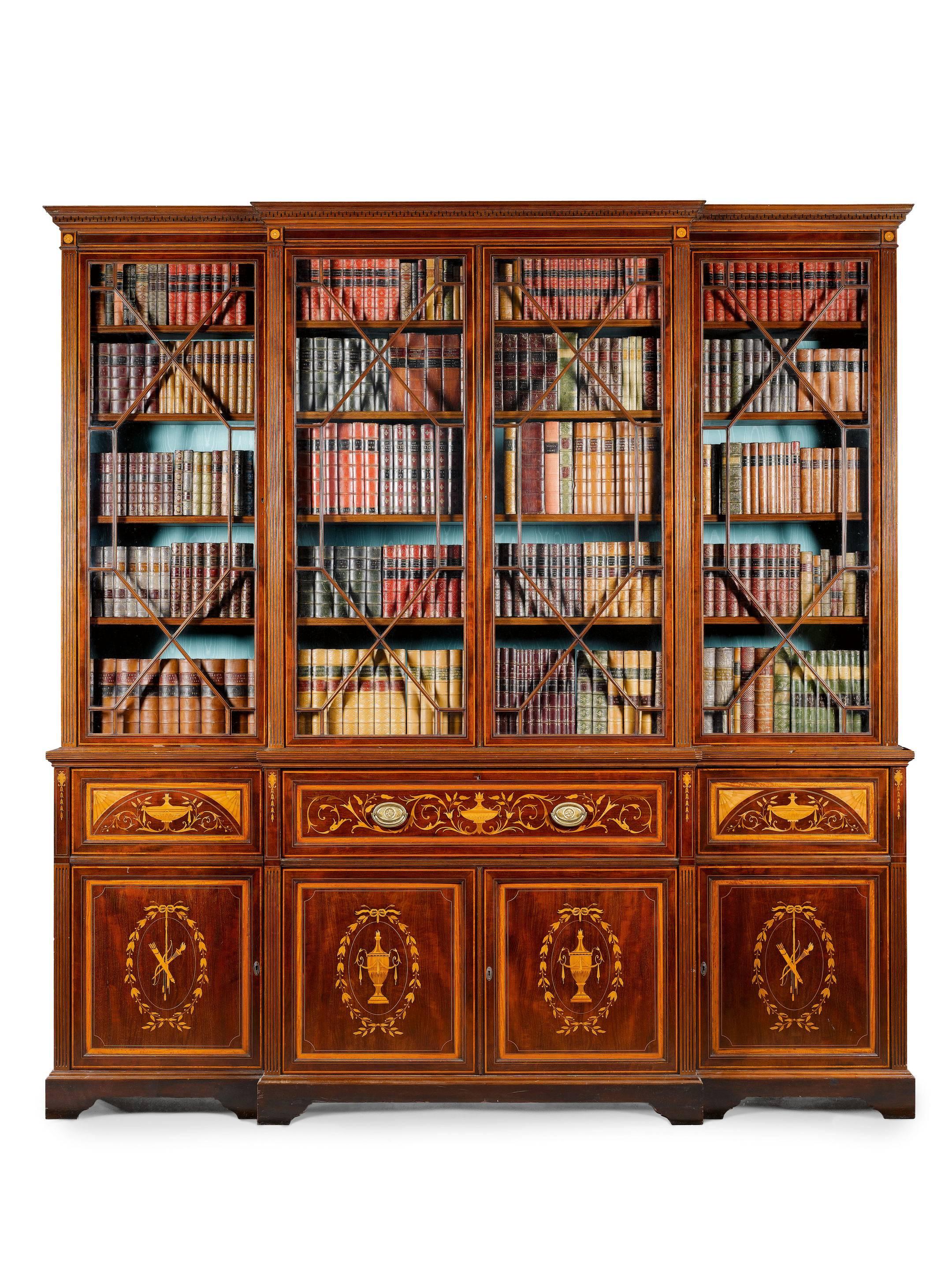 A fine late Victorian mahogany and inlaid Sheraton Revival breakfront bookcase, Edwards and Roberts, London. 

The drawer branded 'Edwards and Roberts,' the moulded cornice with carved geometric pattern and a boxwood strung and inlaid paterae