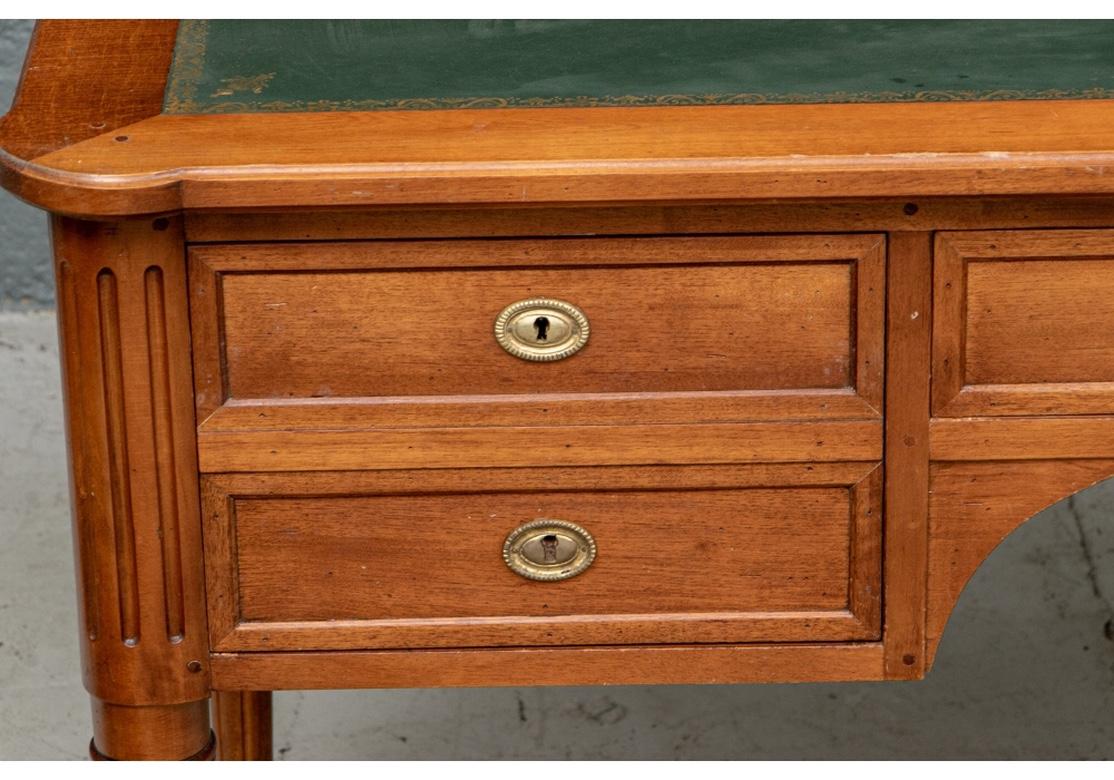 Cherry with rounded corners on the top and tooled matte green inset writing surface. With a knee hole, a center frieze drawer flanked by double drawers on the right, and a single deep drawer on the left. Brass escutcheons (lacking a key). The back