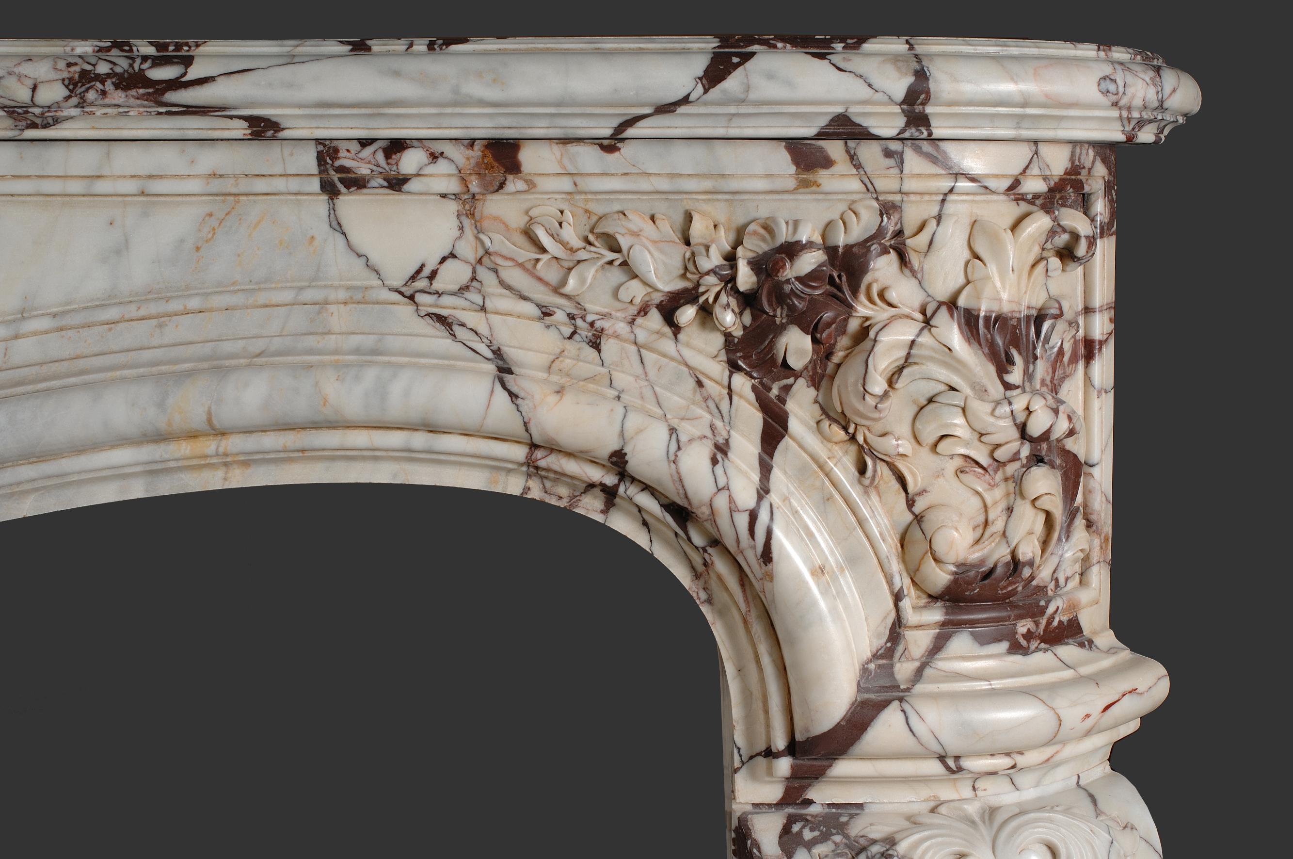 Important et massif  Reproduction d'une cheminée française en marbre de style Louis XV du 18ème siècle. Avec une tablette en forme de serpentin et une frise en arc, décorée de fleurs printanières au centre de la frise et sur les deux côtés du