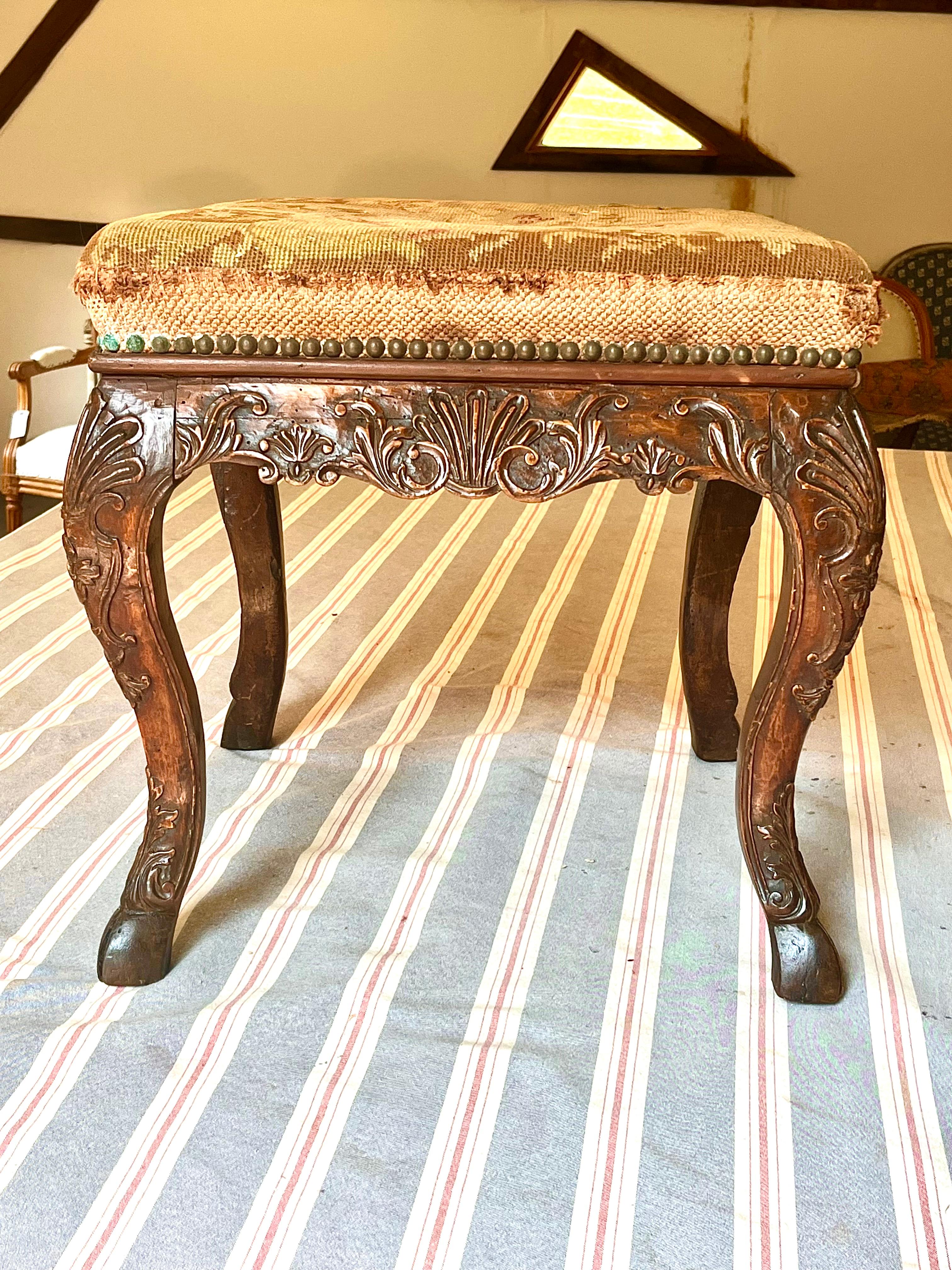 An early Louis XV period tabouret (stool) in walnut, elaborately carved on all four sides with garlands, acanthus leaves, scrolls and other decoration, the scalloped apron supported by cabriole legs, all on carved “pied de biche” (doe’s feet). The