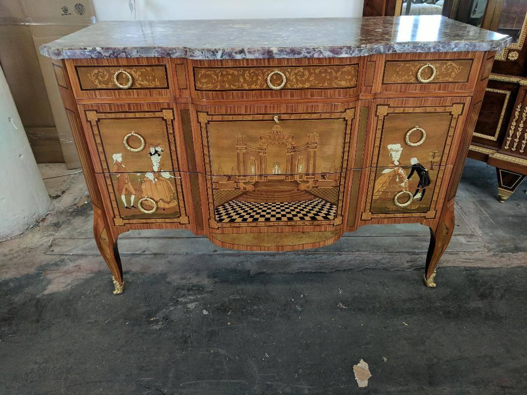 An absolutely exquisite piece of craftsmanship, this antique French commode is done in the Louis XV-XVI transitional style, and is inlaid on all sides, having a three dimensional effect, depicting courting figures and geometric patterns, featuring a