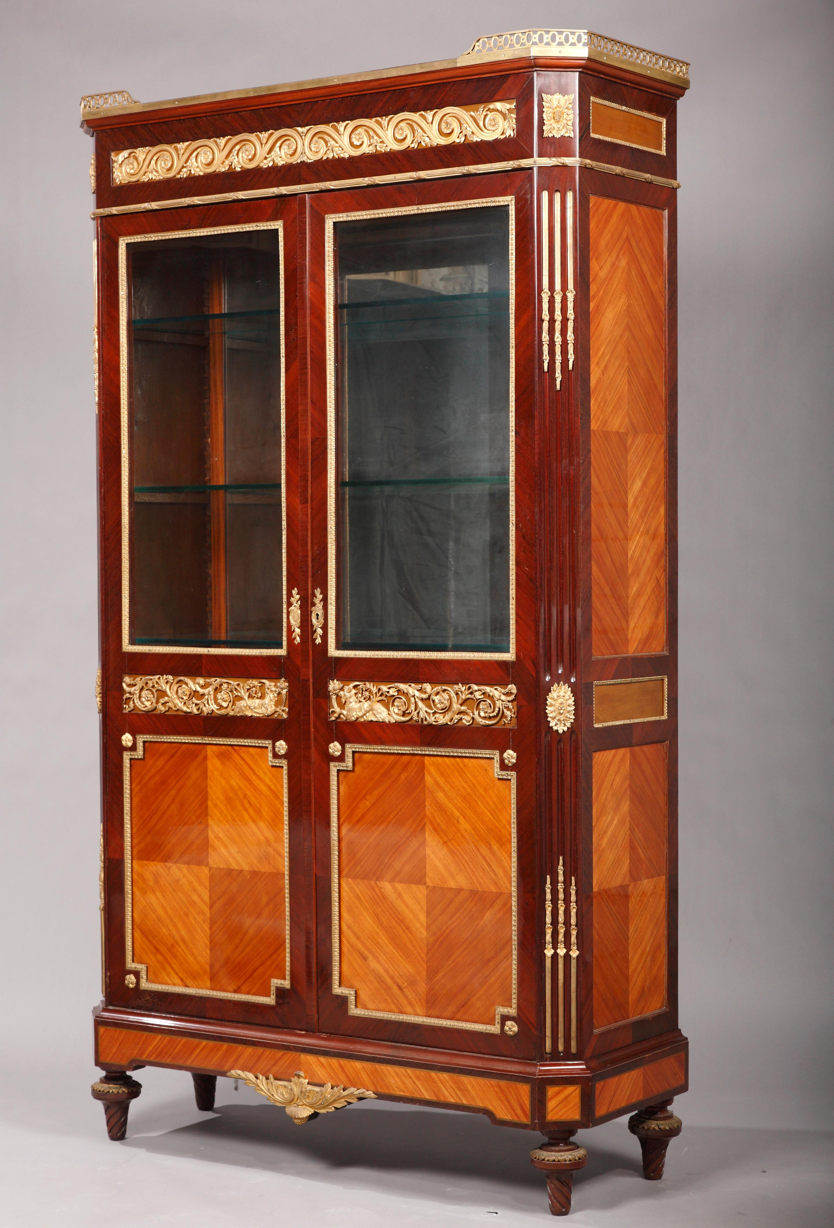 A Louis XVI style vitrine in veneered wood. With two doors glazed at the upper part, opening onto four glass shelves and two drawers. Inner backside fitted with a large mirror. Nicely ornated with rhombus motif on the lower part of the doors as well