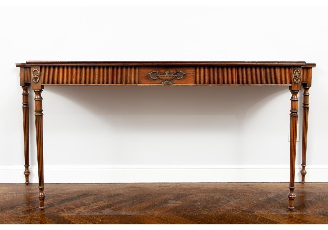 A very refined console table with particularly richly grained wood. Fine mahogany console table with decorative central urn form motif carved in relief. The contoured form console table with a fluted apron and stands on 4 tapered, turned and fluted